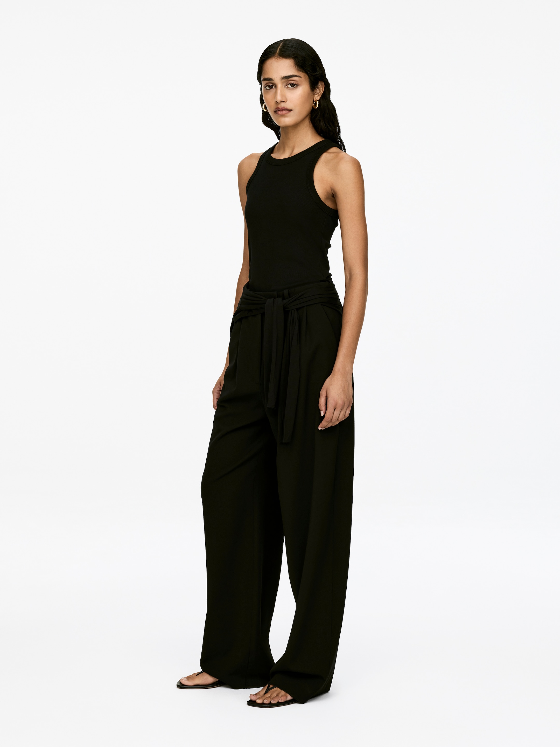 Grösseres Bild ansehen: Ein schwarzes Slim-Fit-Tanktop mit gerippter Jersey-Textur und einem Racer-Ausschnitt wird vom Model getragen.