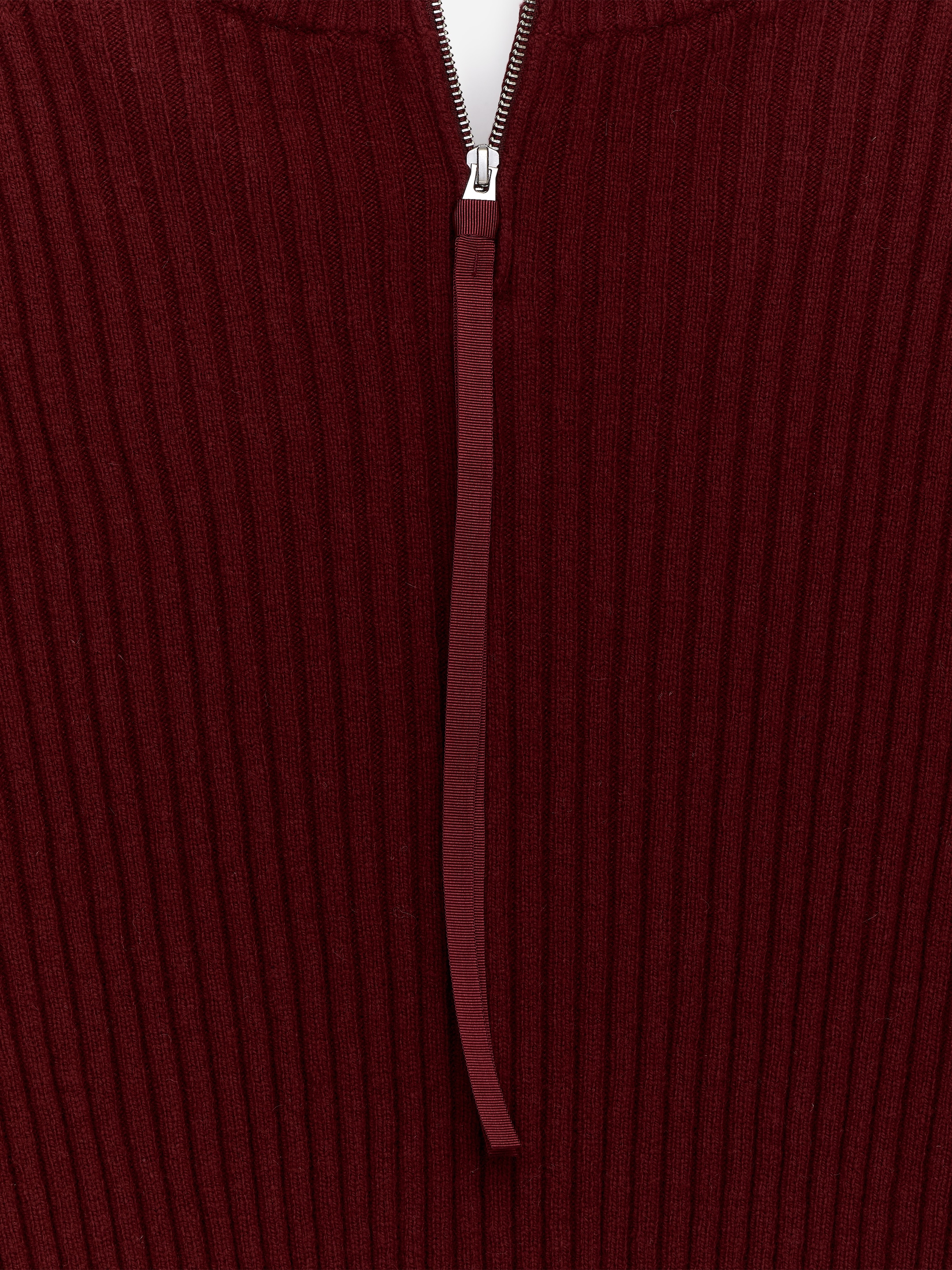 Agrandir l'image: Un vêtement en tricot nervuré d'un rouge profond arbore une fermeture éclair argentée partiellement ouverte sur le devant, avec un tirette en tissu rouge assortie dépassant de la languette de la fermeture éclair et positionnée sur une patte de boutonnage blanche.