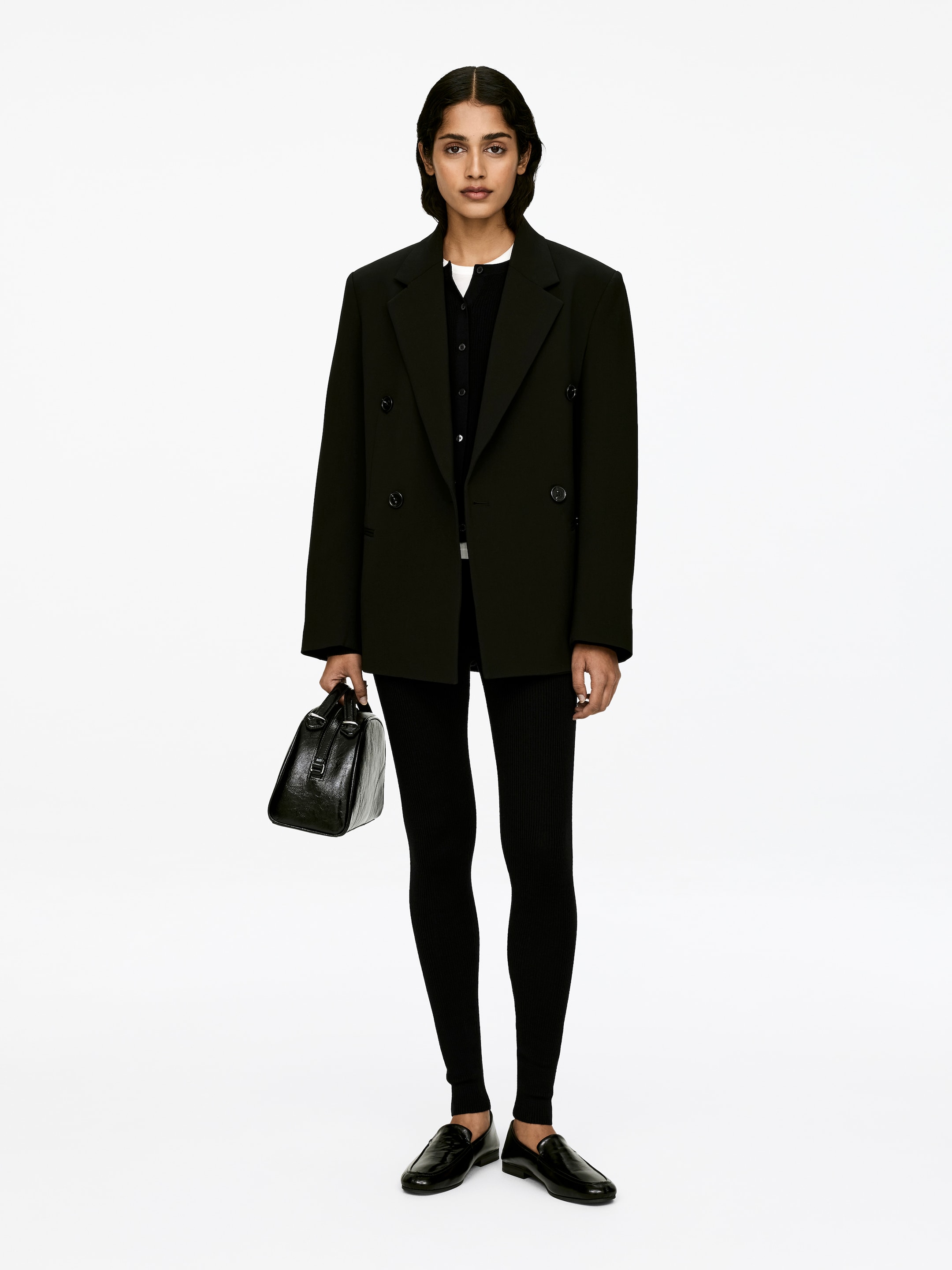 Zobacz większy obraz: Modelka ma na sobie czarne legginsy z prążkowanego dzianiny, charakteryzujące się dopasowanym krojem, wysokim stanem i długością do kostek.