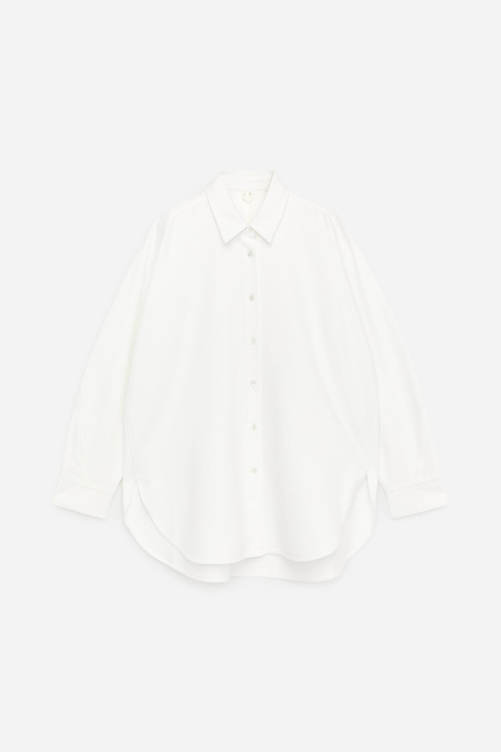 Ver imagem maior: Uma camisa branca de botões, FRONT, apresenta uma gola pontiaguda, mangas compridas com punhos abotoados, uma carcela frontal com botões visíveis e uma bainha arredondada.