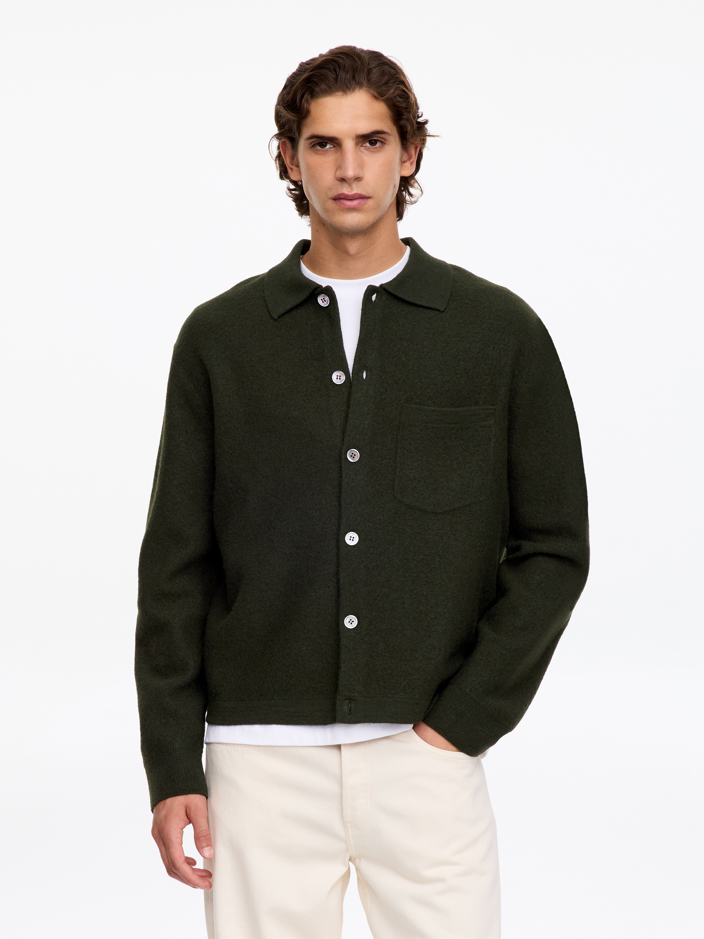 A dark green knitted overshirt is shown from the front, featuring a classic collar, a button-down front with six light-coloured buttons, and a single patch pocket on the left chest.