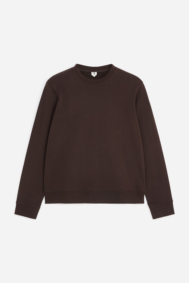 En mörkbrun sweatshirt med rund hals är vänd framåt och visar en normal passform. Sweatshirten har långa ärmar med ribbade muddar, en ribbad rund halsringning och en matchande ribbad nederkant. - 1