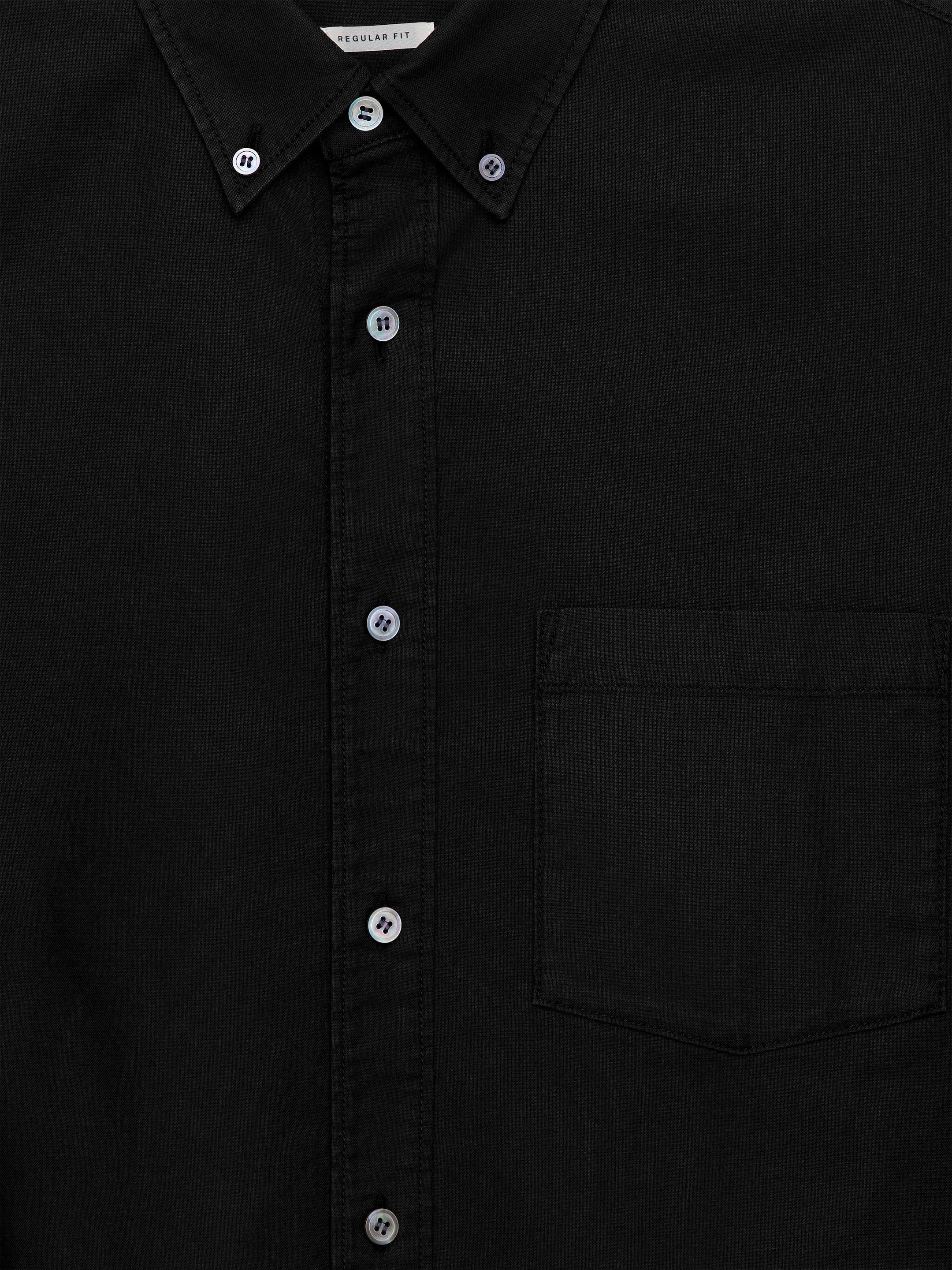 Ver imagen más grande: Una camisa negra de tejido Oxford se presenta en la parte DELANTERA, con un cuello con botones y una tapeta de botones delanteros, ambos asegurados con botones de nácar iridiscentes. Un solo bolsillo de parche en el pecho es visible en el lado izquierdo del usuario.