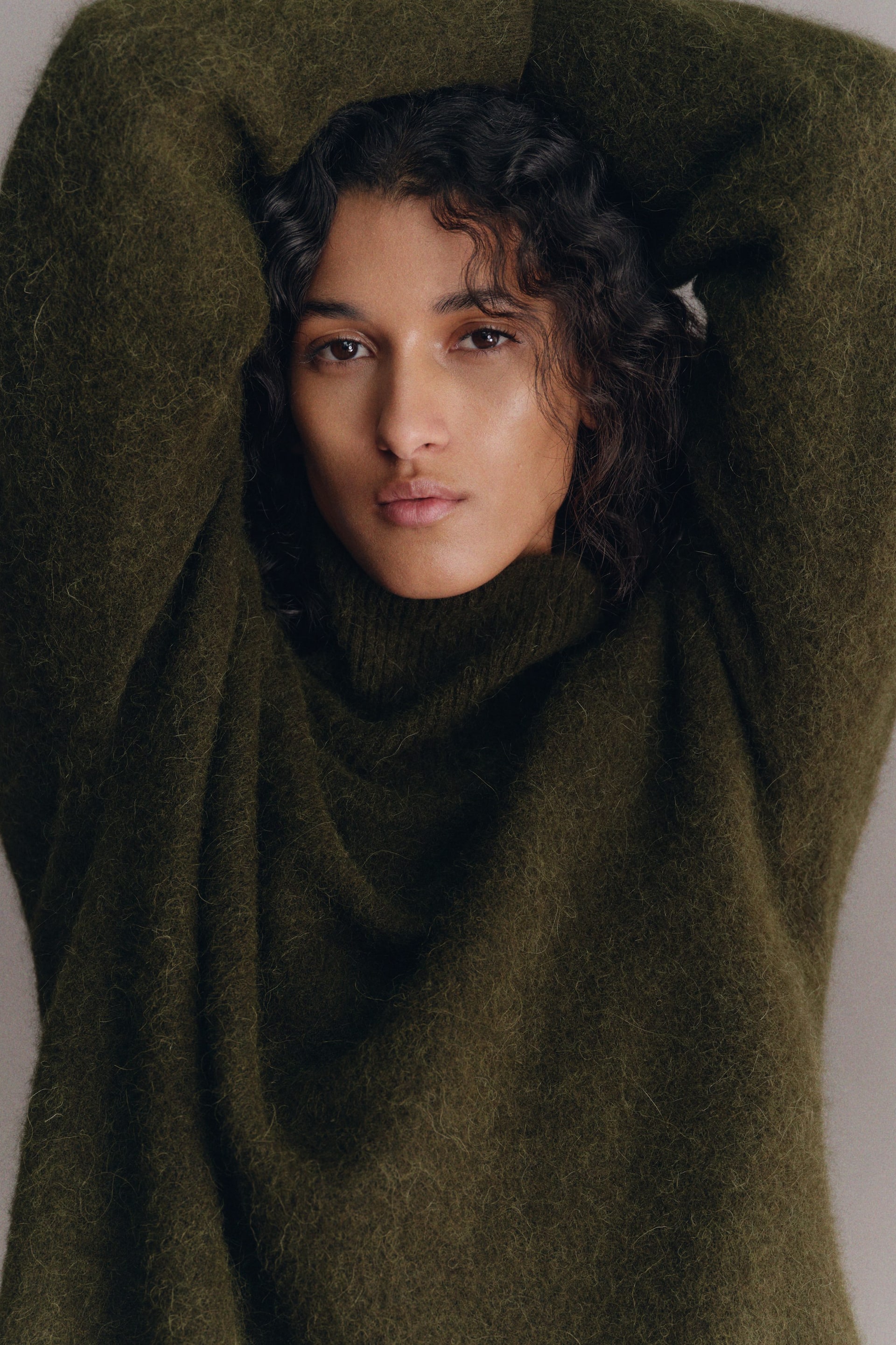 Größeres Bild anzeigen: Ein dunkelgrüner, flauschiger Strickpullover wird von vorne präsentiert und zeigt seinen hohen Kragen. Die langen, lockeren Ärmel werden angehoben, um die weiche, flauschige Strickstruktur hervorzuheben.