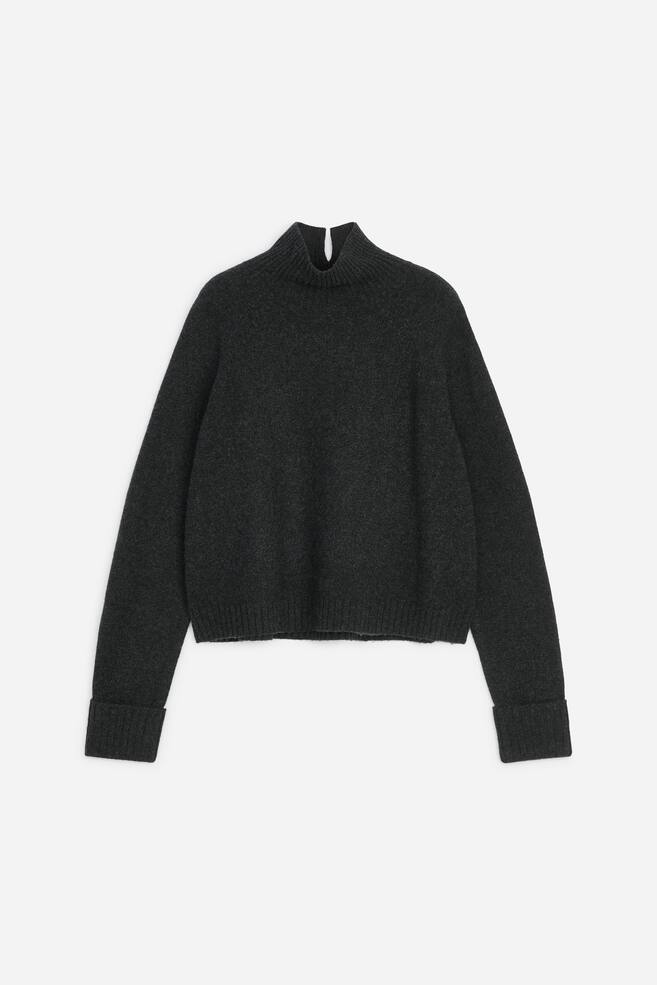 A dark grey knitted roll-neck jumper is shown from the front in a regular fit, featuring long raglan sleeves with wide folded ribbed cuffs and a matching ribbed hem. The high ribbed collar features a small vertical slit at the centre. - 1