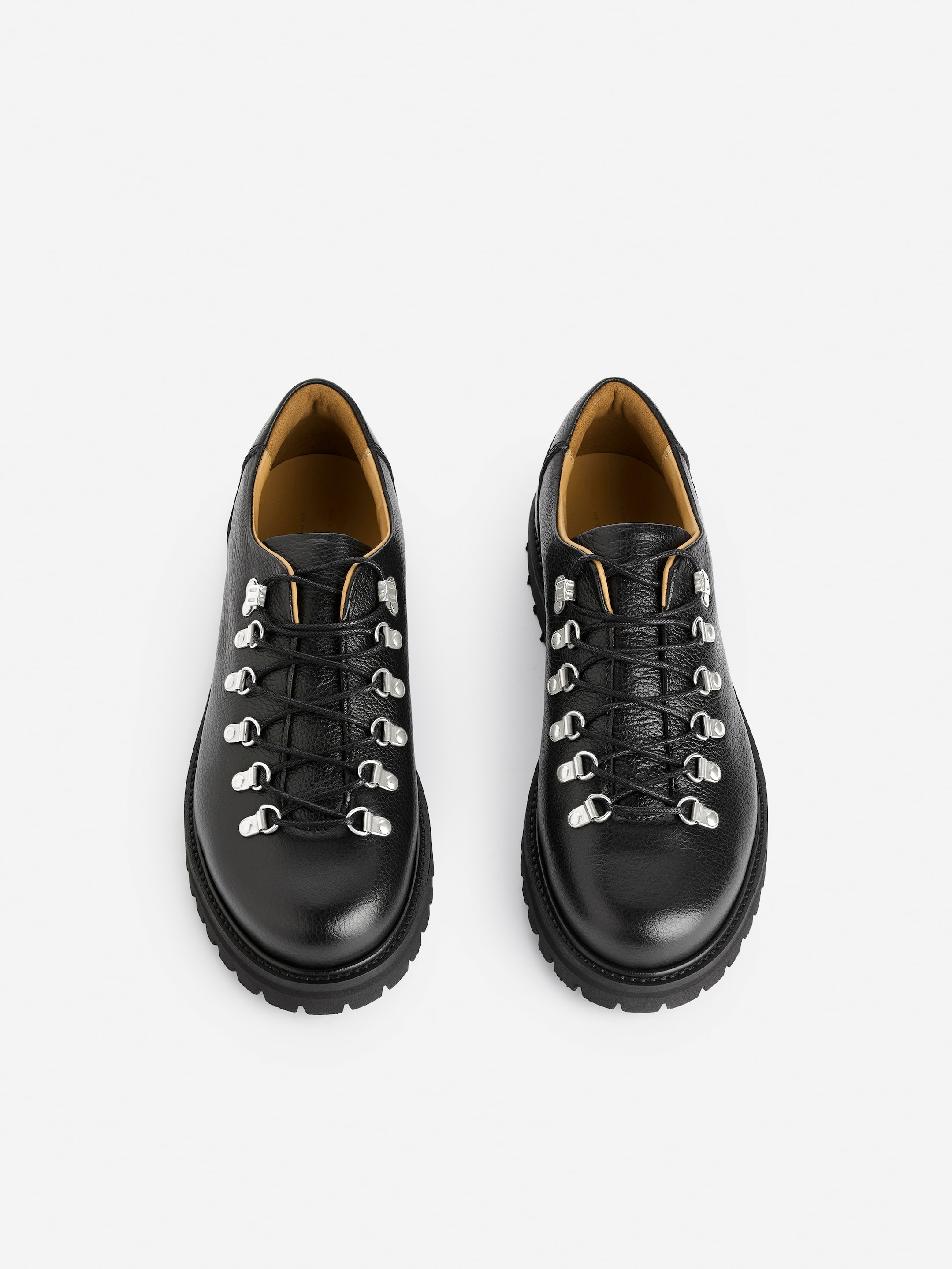 Grösseres Bild ansehen: Ein Paar schwarze Wanderschuhe sind nach VORNE ausgerichtet, zeigen genarbtes Leder und ein Schnürdesign mit schwarzen gewachsten Schnürsenkeln, die durch Schlaufenösen aus Gunmetall laufen. Eine weich gepolsterte Zunge und ein gepolsterter Kragen sorgen für Komfort, während eine hellbraune Ledersohle sichtbar ist, und die Schuhe sind mit robusten Gummiprofilsohlen ausgestattet.