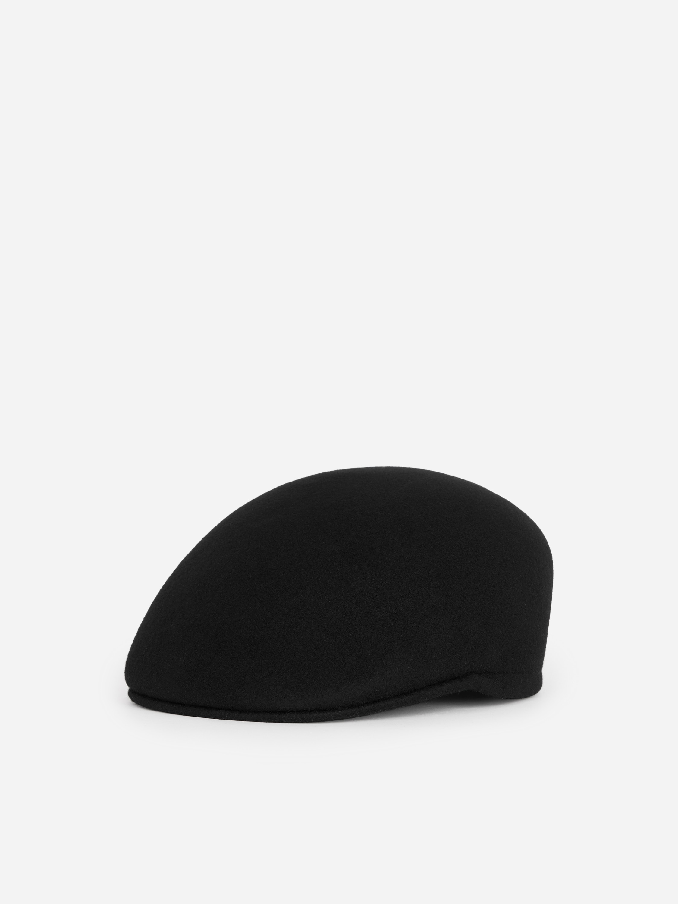 A black wool flat cap with a structured, classic silhouette is being worn by the model, who is shown in profile. The cap is styled with a high-collared, textured black coat.