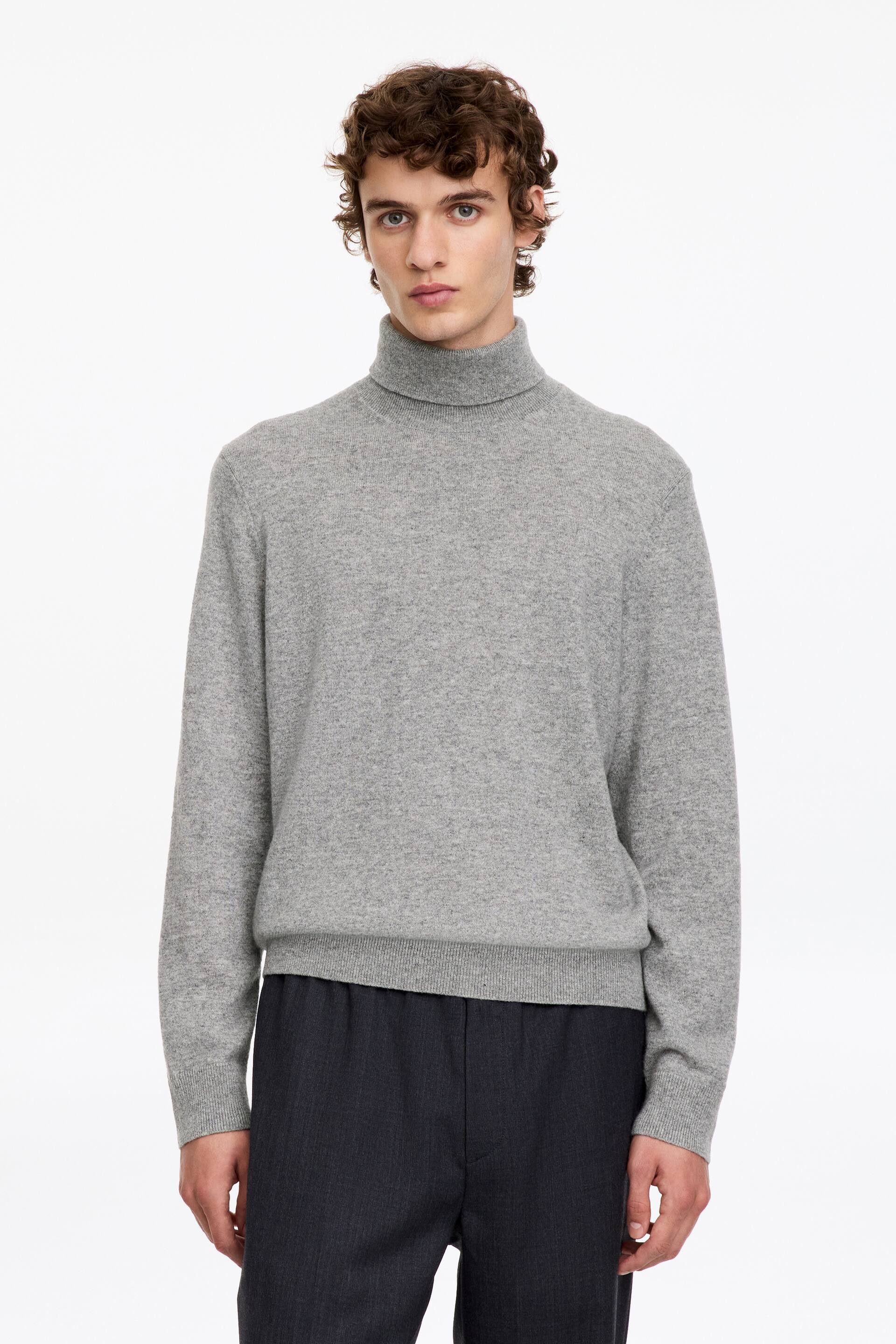 Agrandir l'image: Un pull à col roulé gris clair est porté par le mannequin, avec une maille unie et un col, des poignets et un ourlet côtelés. Le pull est associé à un pantalon gris foncé.