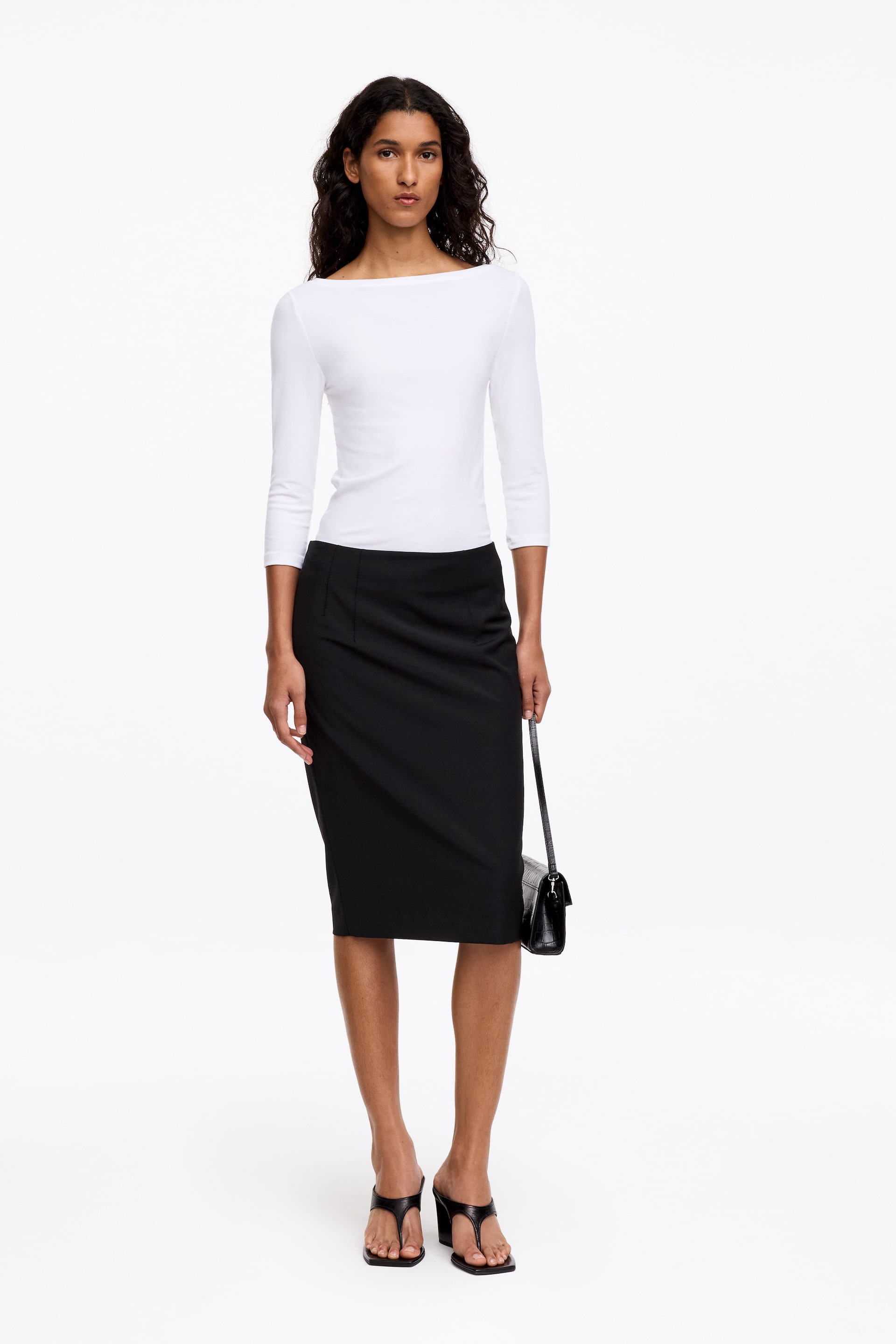 View larger image: A black wool-blend pencil skirt is being worn by the model, featuring a knee-length cut and front dart detailing. The skirt is styled with a white three-quarter-sleeve top tucked into the waistband.