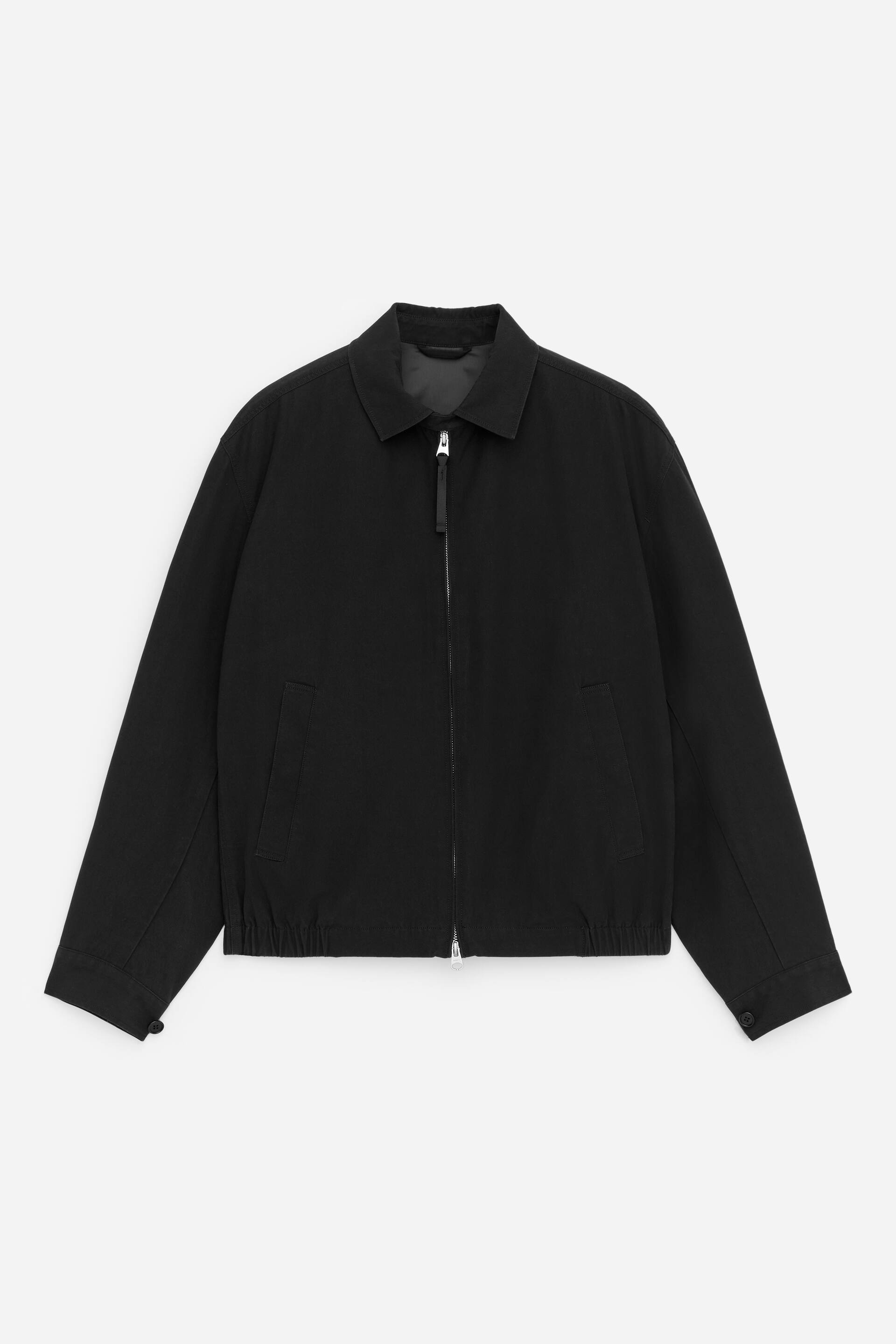 Se større billede: En sort blousonjakke præsenterer sin FORSIDE, med en almindelig krave, en tovejs lynlåslukning, skrå paspolerede lommer, knappede manchetter og en elastisk bundkant.