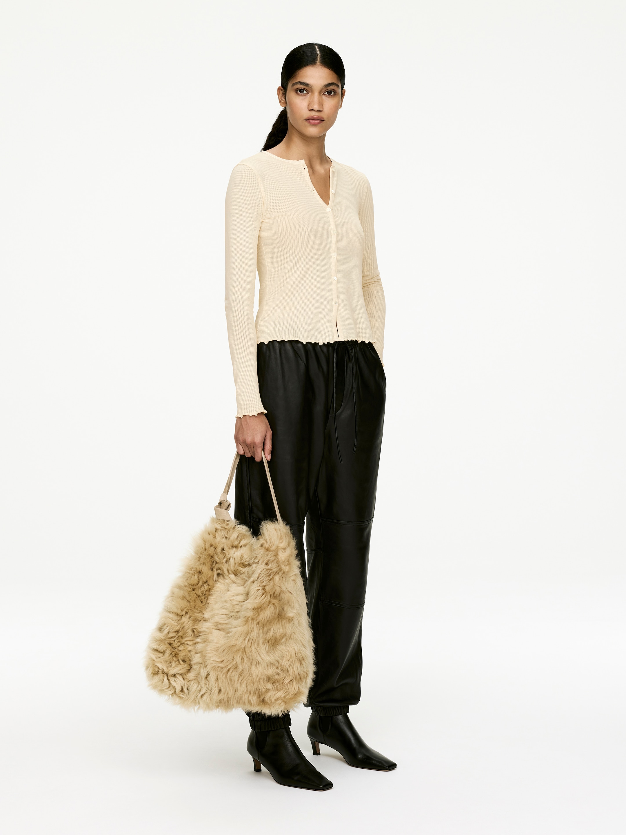 Agrandir l'image: Un sac en fourrure marron clair et hirsute est tenu par une fine sangle de couleur claire, orienté légèrement vers l'avant. Le sac présente une forme pleine, irrégulière et décontractée.