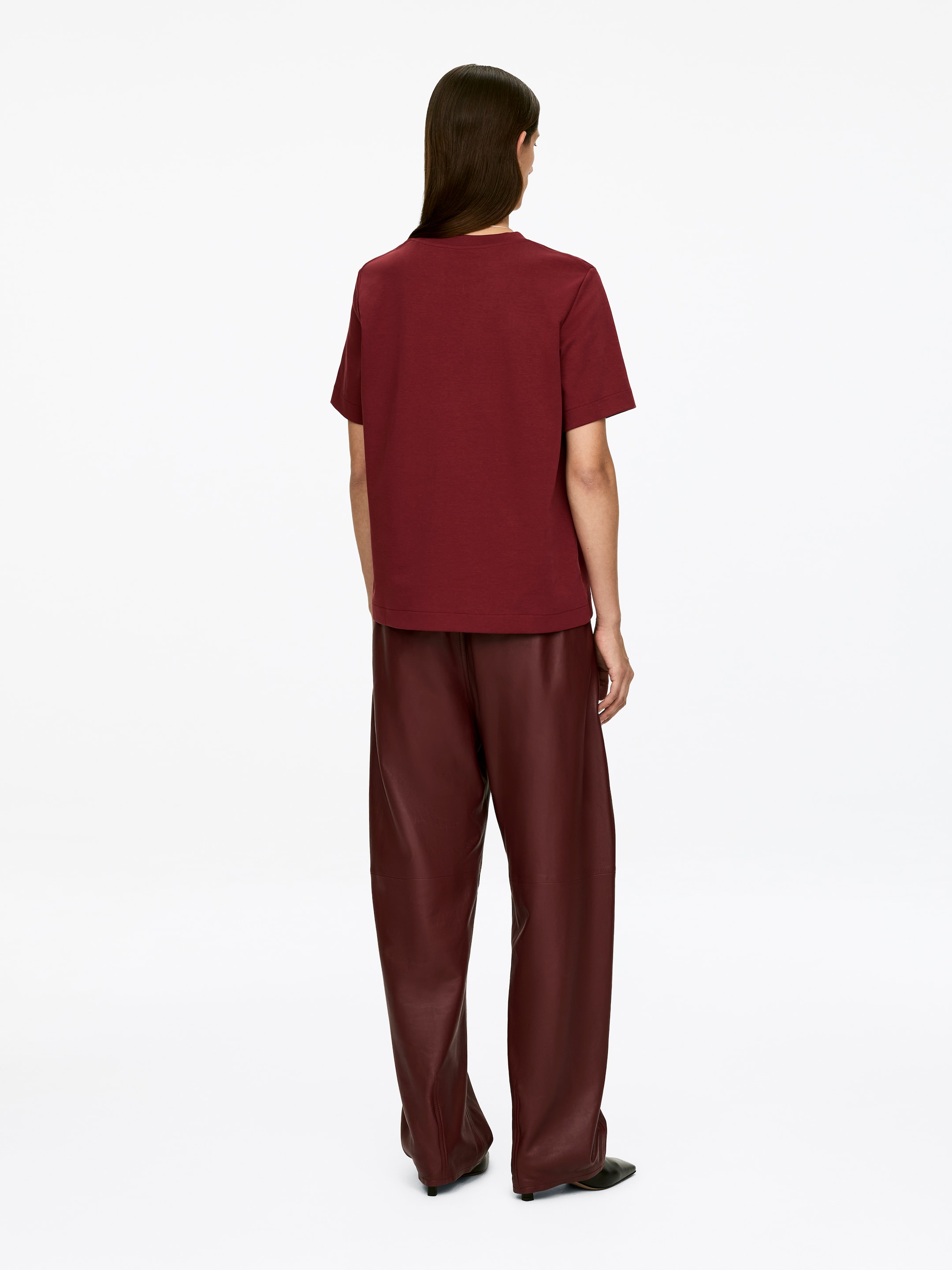 Visa större bild: En djupröd T-shirt, med rund hals och mjukt skräddade korta ärmar, bärs av modellen. T-shirten har en normal passform och kombineras med vida byxor i en liknande djupröd färg.
