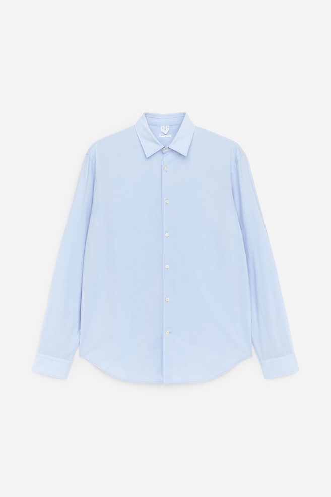 O produto é uma camisa de popelina azul clara apresentada de frente, com uma gola clássica e uma carcela de botões frontais com botões de cor clara. Também exibe mangas compridas com punhos abotoados e uma bainha curva. - 1