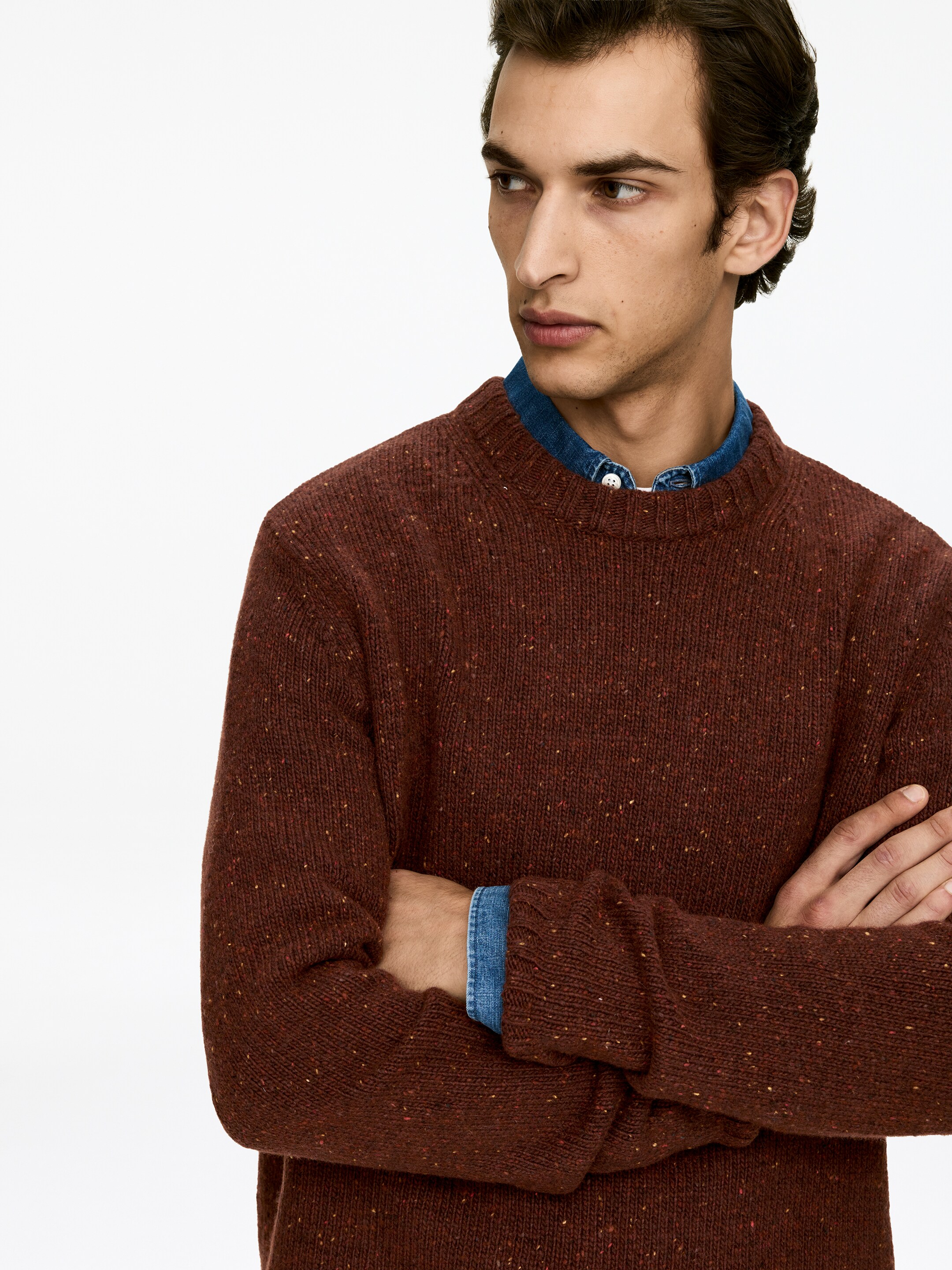 Ver imagen más grande: Un jersey de cuello redondo marrón moteado se está utilizando desde un ángulo frontal, mostrando su tejido texturizado con pequeñas motas de colores, y superpuesto sobre una camisa de mezclilla azul con cuello visible en el escote y los puños.