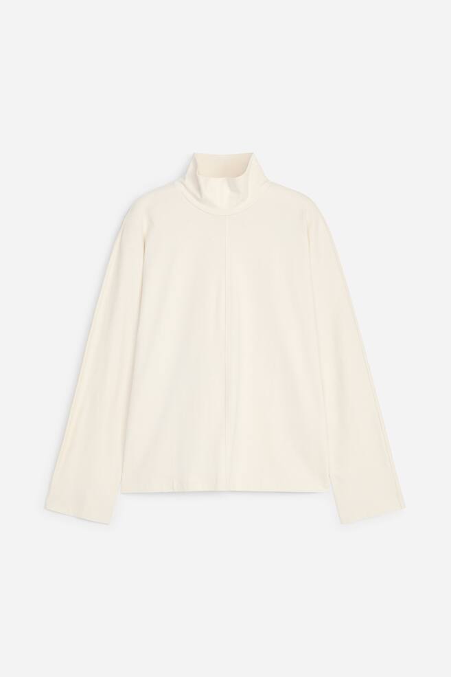 A cream-coloured, long-sleeved top is shown from the front, featuring a relaxed silhouette with wide batwing sleeves, a high roll neck, and a vertical centre seam running down the front. - 1