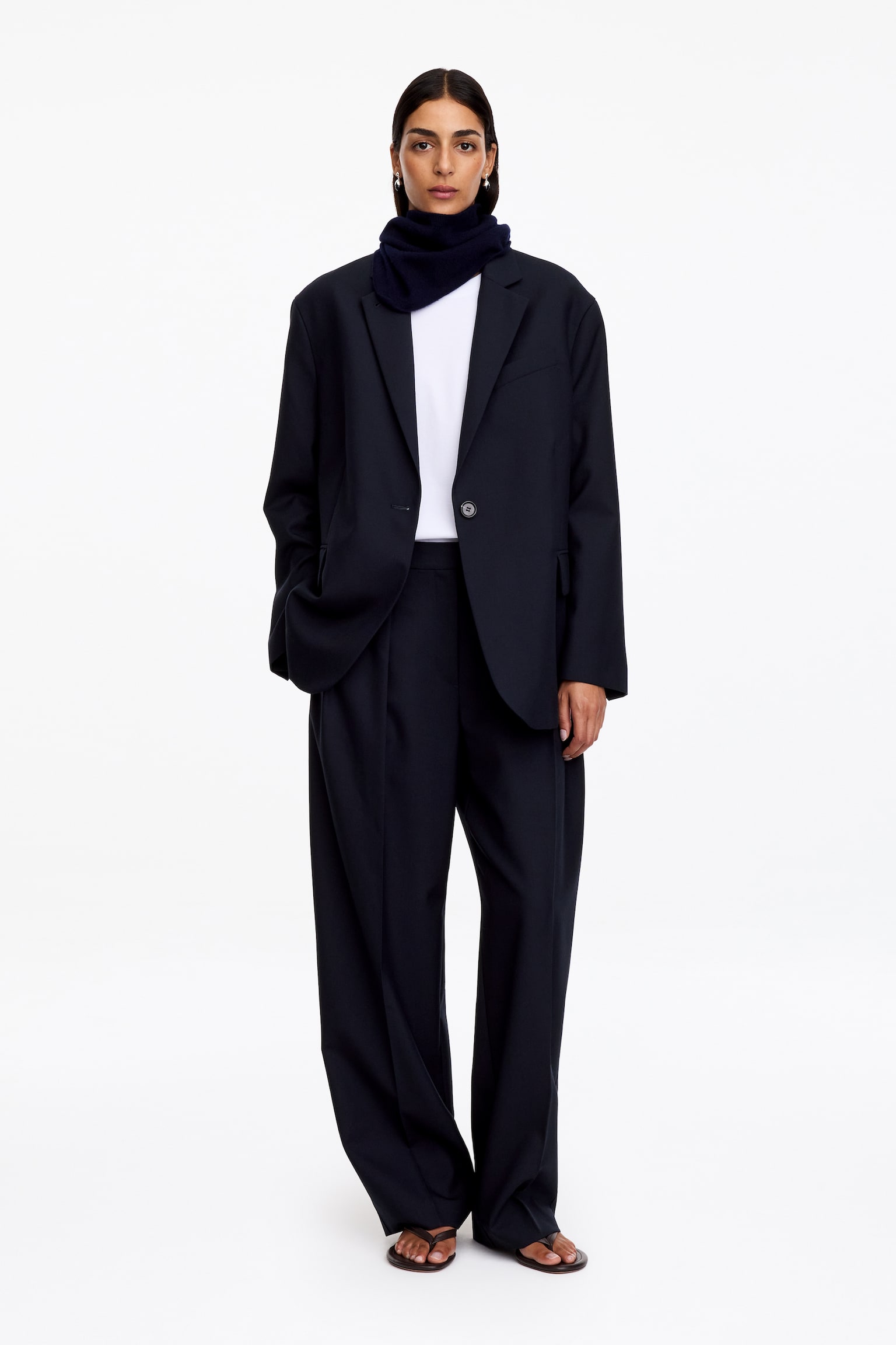 Um blazer azul-marinho de abotoamento simples está de frente, exibindo uma silhueta de corte descontraÃdo com ombros bem definidos e lapelas clássicas. O casaco apresenta um fecho de um botão, um bolso de peito embutido e dois bolsos com pala espaçosos. - 1