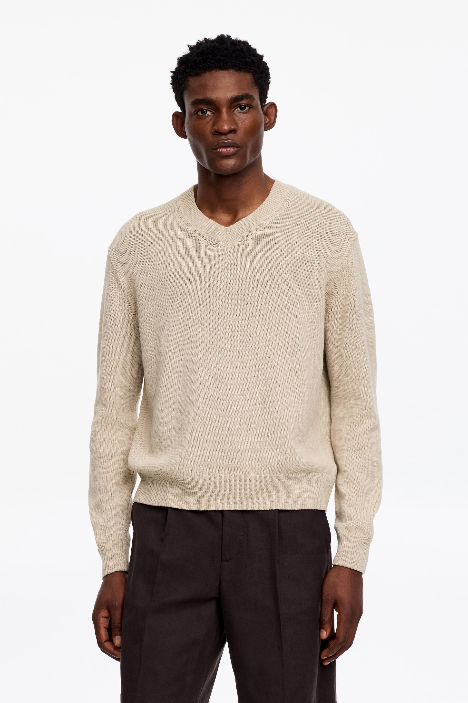 Visualizza immagine più grande: Un maglione beige con scollo a V è presentato frontalmente, caratterizzato da uno scollo a V a coste, maniche lunghe con polsini a coste e un orlo a coste. Il maglione presenta una trama a maglia fine.