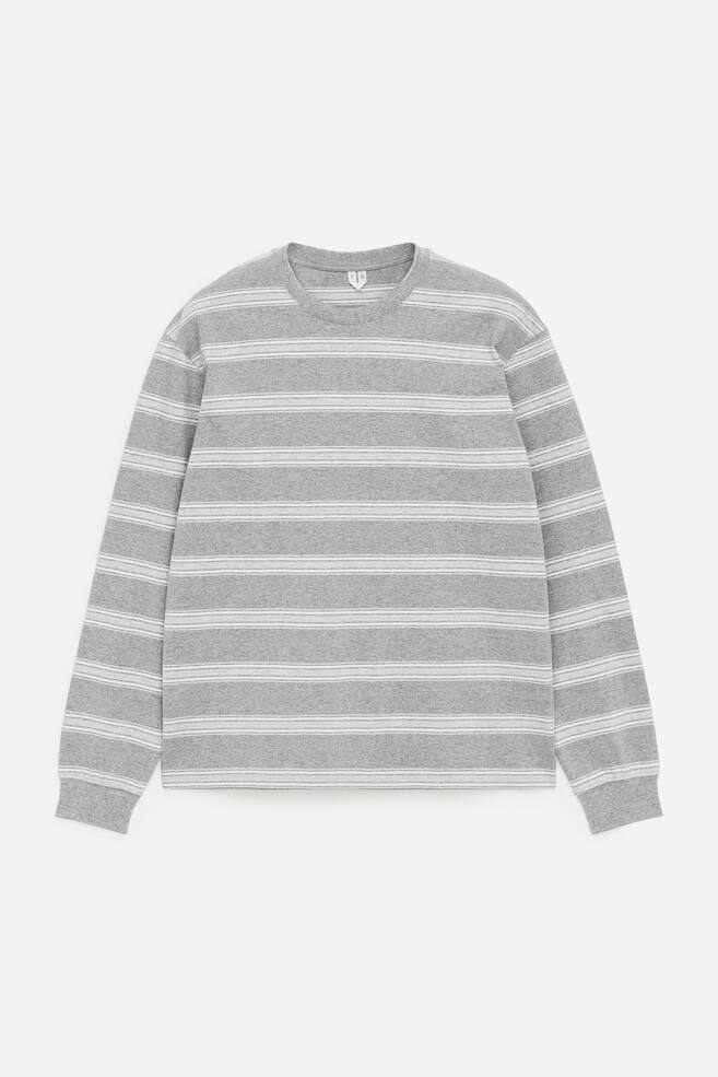 Una camiseta de manga larga presenta su parte delantera, con una base gris y rayas horizontales blancas de diferentes anchos. Está diseñada con un cuello redondo y acabados de canalé en el cuello y los puños, mostrando un ajuste relajado. - 1