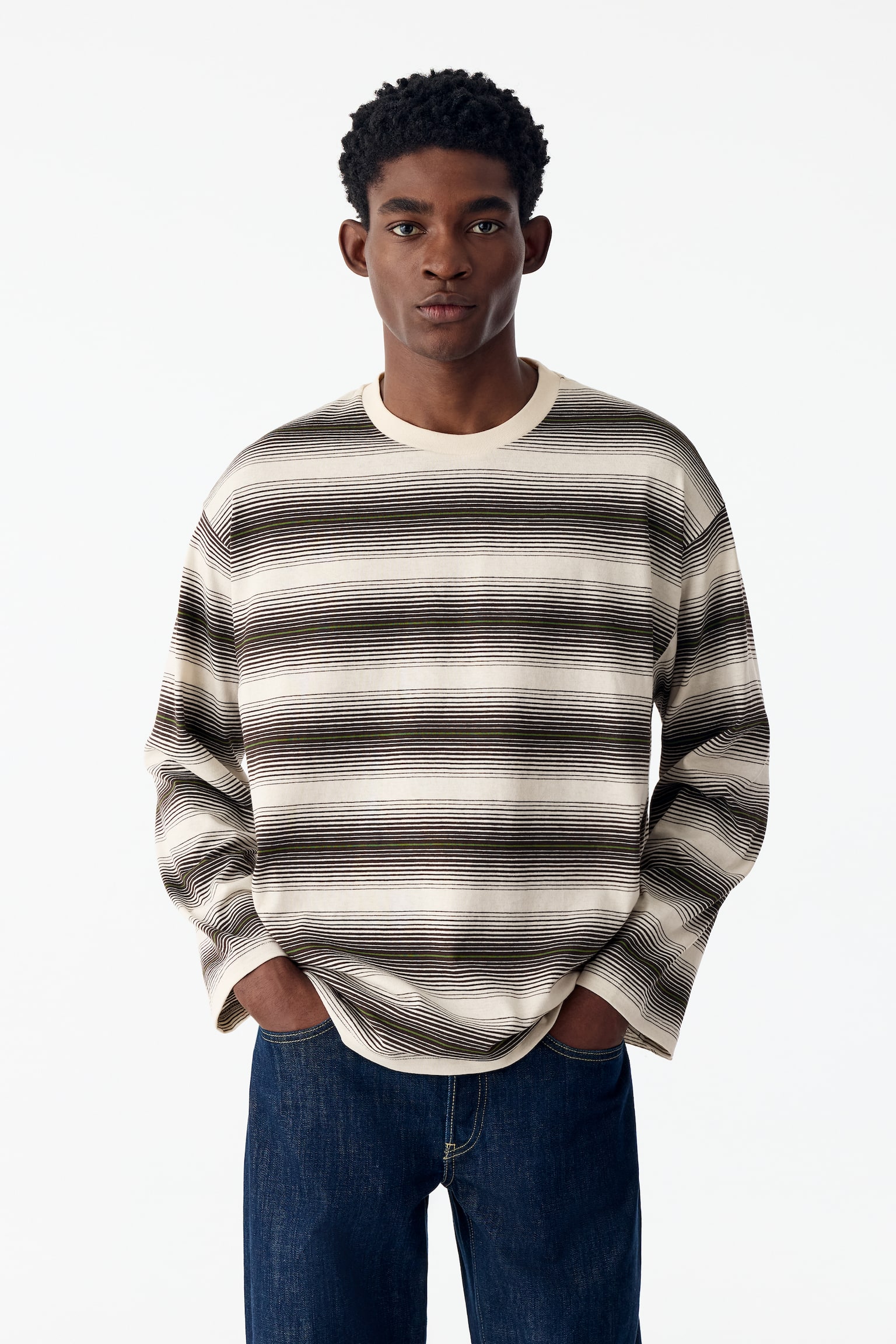 Se muestra una camiseta de manga larga vista de frente, con un patrÃ³n horizontal de rayas teÃ±idas en hilo en color crema, marrÃ³n oscuro y verde oliva. La prenda de corte relajado presenta cuello redondo acanalado en color crema, mangas largas anchas y bajo recto. - 1