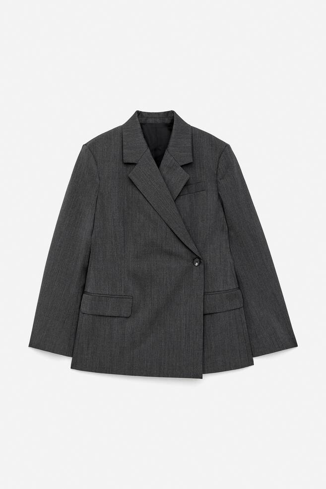 Un blazer avvolgente su misura viene presentato FRONT, realizzato in lana grigio scuro con una trama leggermente testurizzata. Presenta revers a tacca, una chiusura a un bottone, un taschino sul petto e due tasche con patta inferiori, con spacchi a cucitura a pannello visibili sui lati. - 1