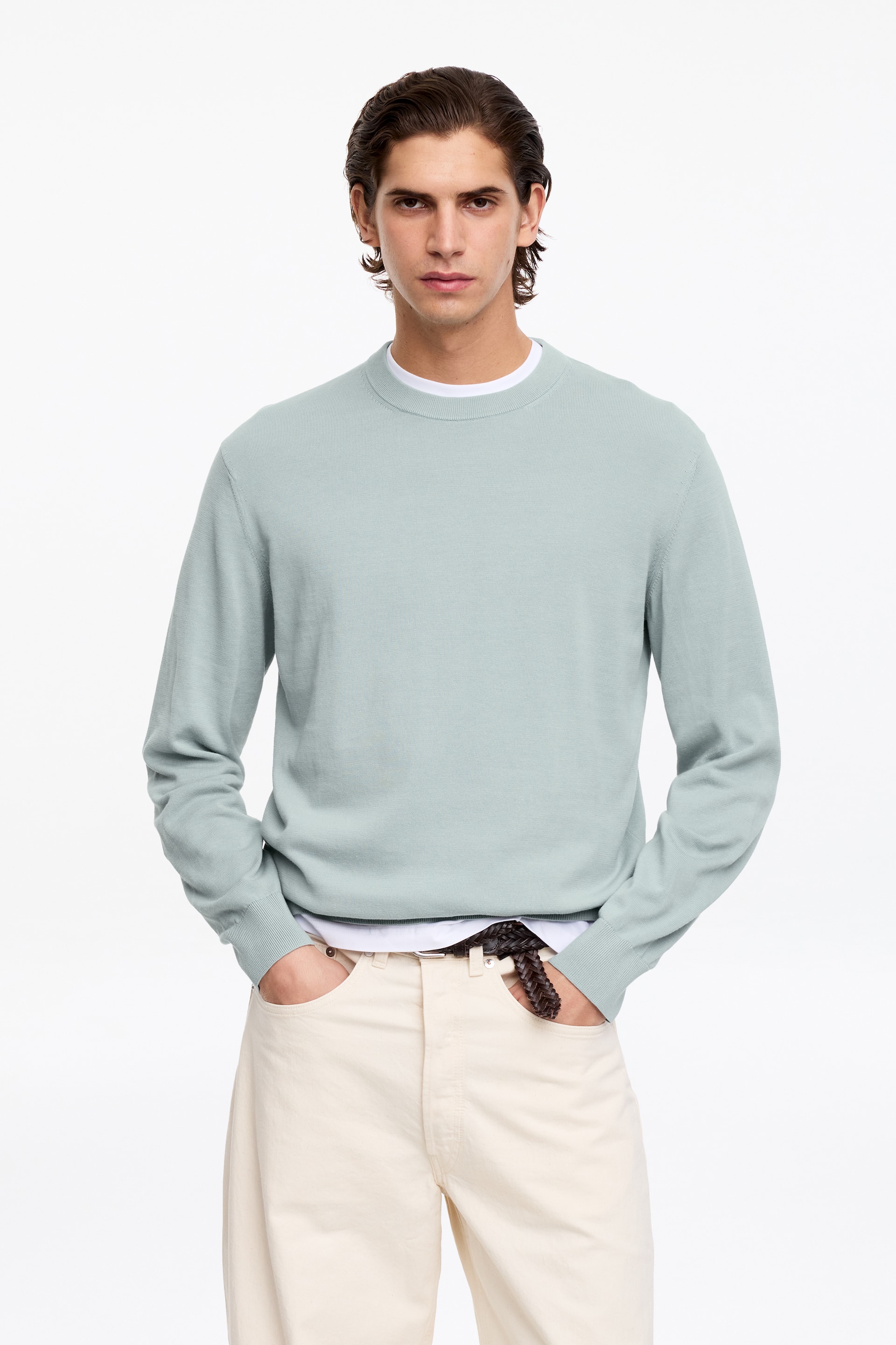 Visa större bild: En ljus salviagrön tröja med rund hals presenteras, med ribbad krage, långa ärmar med ribbade muddar och en ribbad fåll. Den är lagrad över en vit t-shirt, synlig vid halsringningen och fållen.
