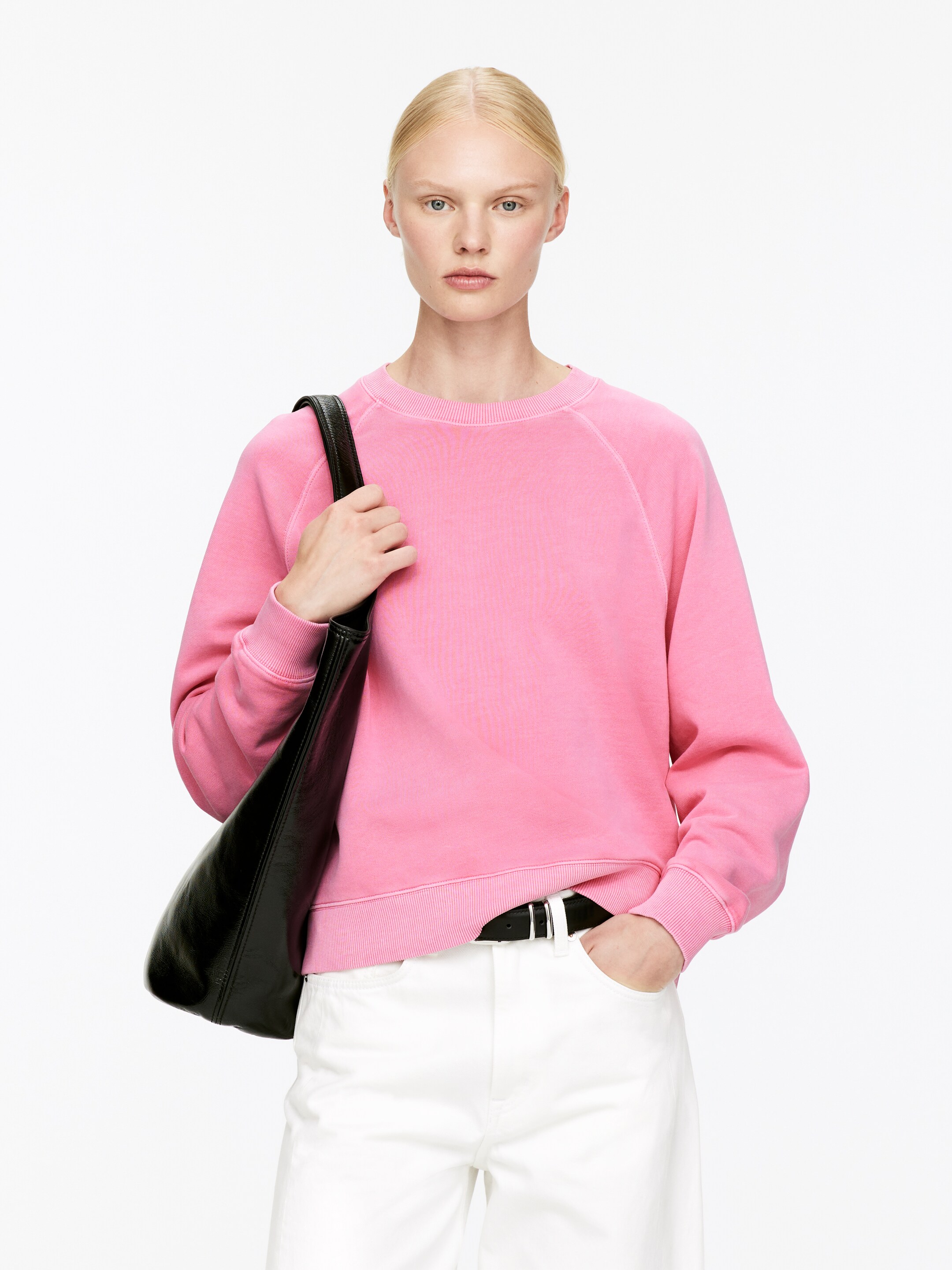 Größeres Bild anzeigen: Ein rosa Sweatshirt mit Rundhalsausschnitt wird getragen, das Raglanärmel, gerippte Bündchen und einen gerippten Saum aufweist. Es ist mit weißen Hosen und einem schwarzen Gürtel gestylt, während eine schwarze Tasche auf der Schulter ruht.