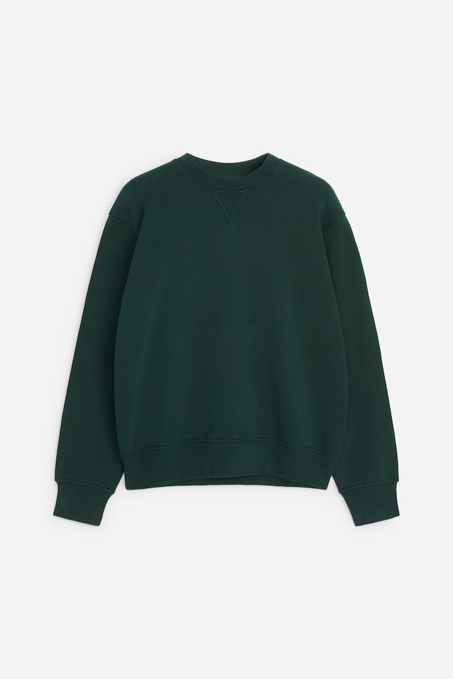 Una felpa girocollo verde scuro è mostrata frontalmente, con il classico inserto a V cucito sulla scollatura. Il capo presenta maniche lunghe con spalle scese, polsini a coste e un orlo a coste coordinato. - 1