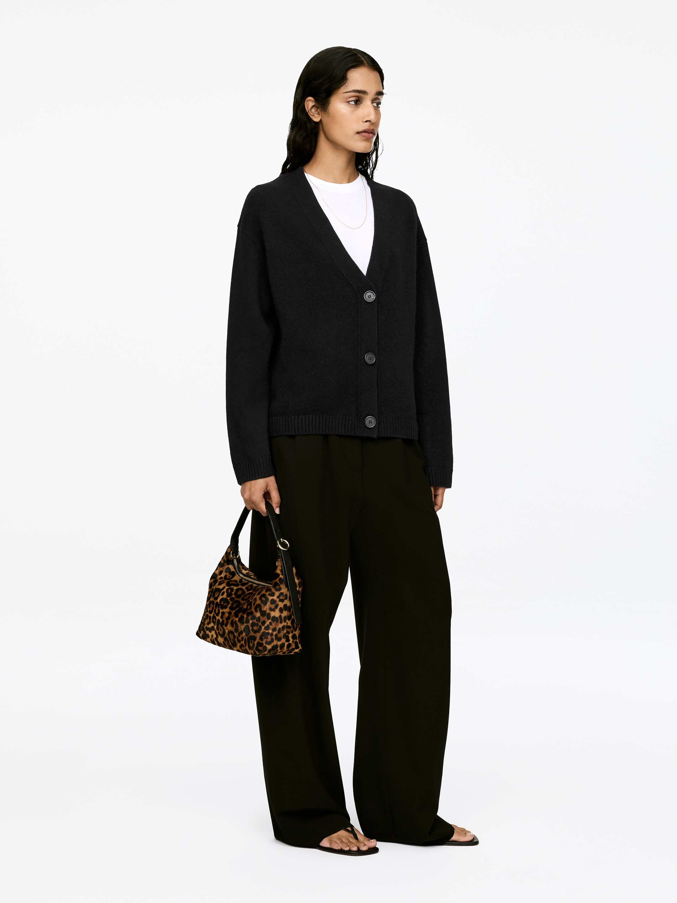 View larger image: A black long-sleeved cardigan, featuring a V-neck, button closure, and rib-knitted trims, is being worn by the model. The cardigan is partially buttoned, layered over a white t-shirt.