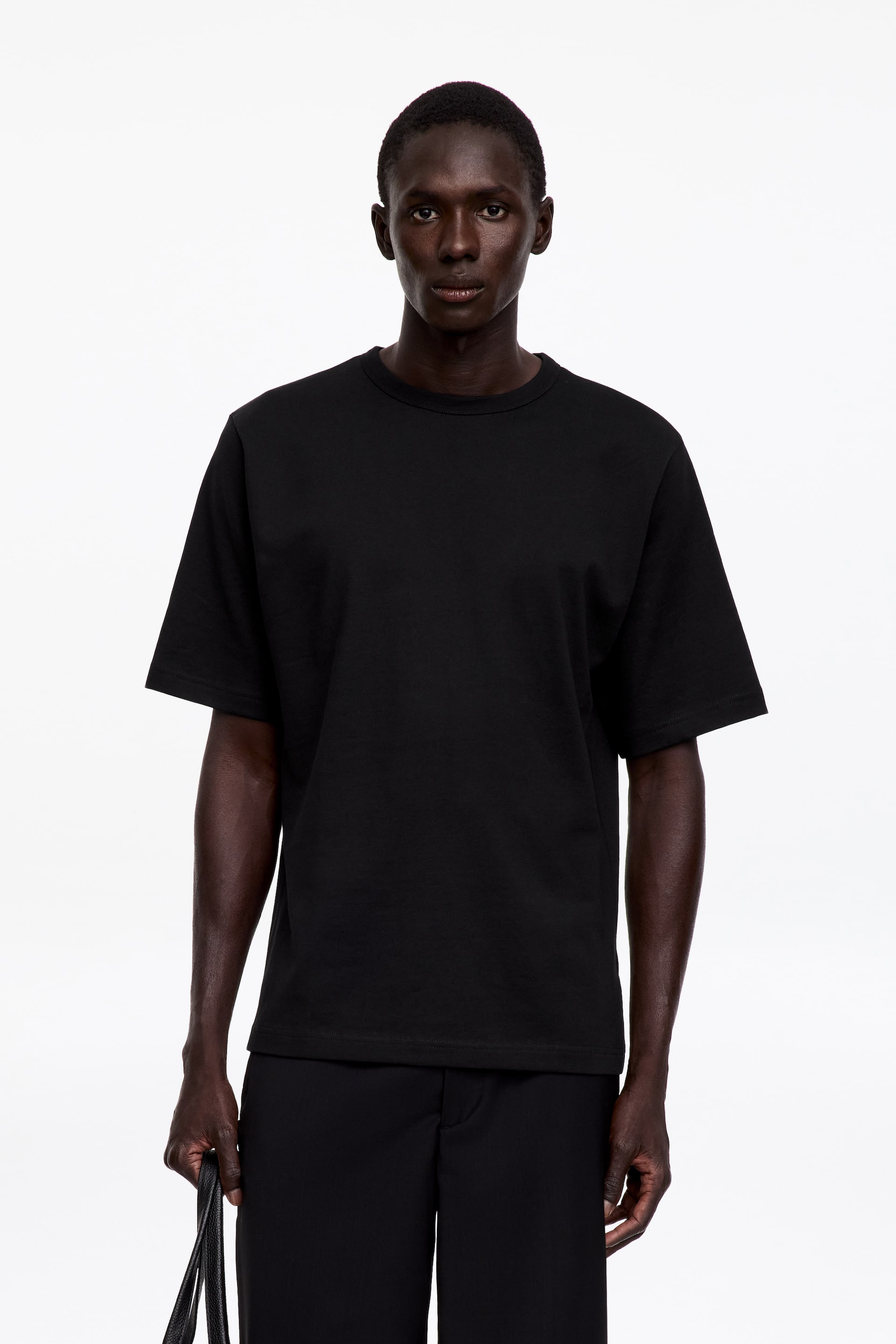 View larger image: The model is wearing a black crew neck T-shirt. It features an oversized silhouette with longer sleeves, a generous cut through the body, and 1x1 rib binding at the neck.