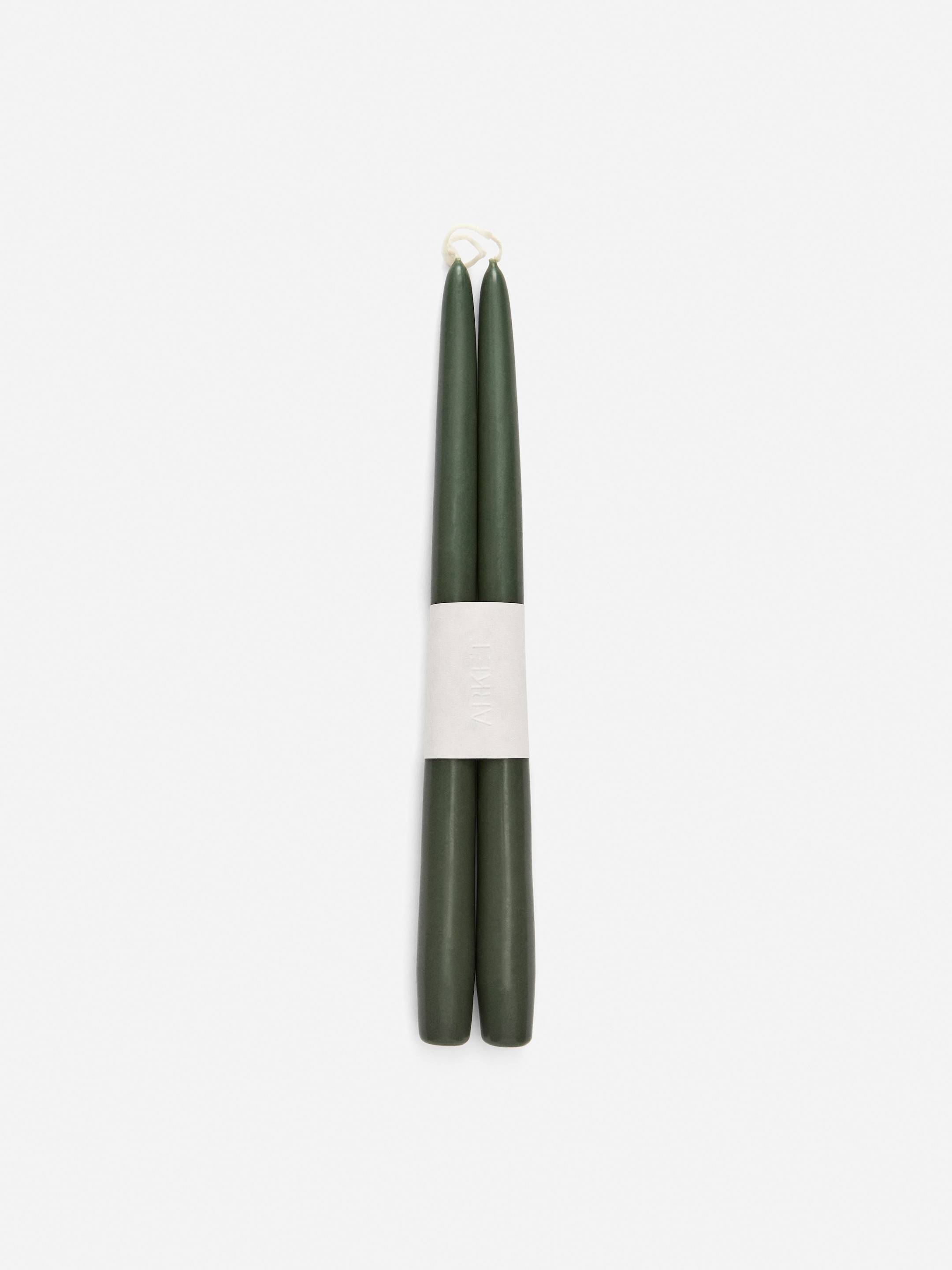 Ver imagen más grande: Dos velas cónicas de color verde oscuro están de pie, unidas por una banda blanca. Una mecha de color claro es visible en la parte superior de cada vela.
