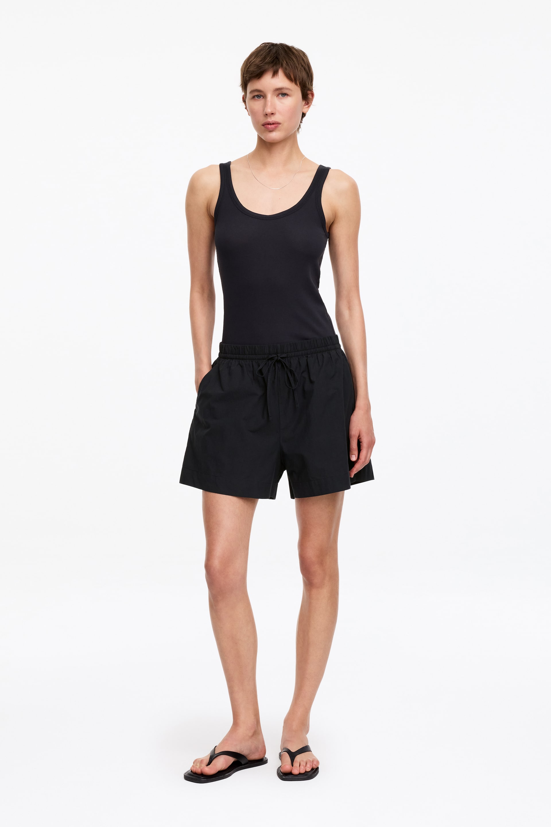 Ver imagen más grande: La camiseta sin mangas negra presenta un escote redondo y tirantes anchos, ajustándose cómodamente. Los pantalones cortos negros ofrecen un ajuste relajado con una cintura elástica con cordón y bolsillos laterales visibles.
