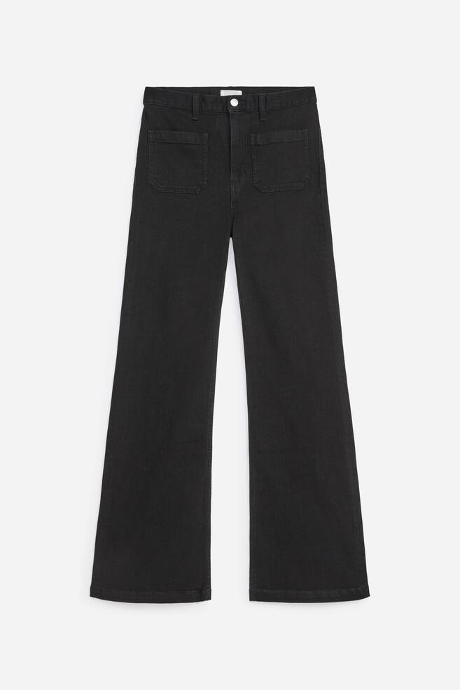 Een paar zwarte wide-leg jeans wordt van voren getoond, met een hoge taille met riemlussen, een zilverkleurige knoopsluiting en twee grote vierkante opgestikte zakken op de heupen aan de voorkant. De denimstof loopt naar beneden uit in een uitlopende, wide-leg silhouet met netjes afgewerkte zomen. - 1