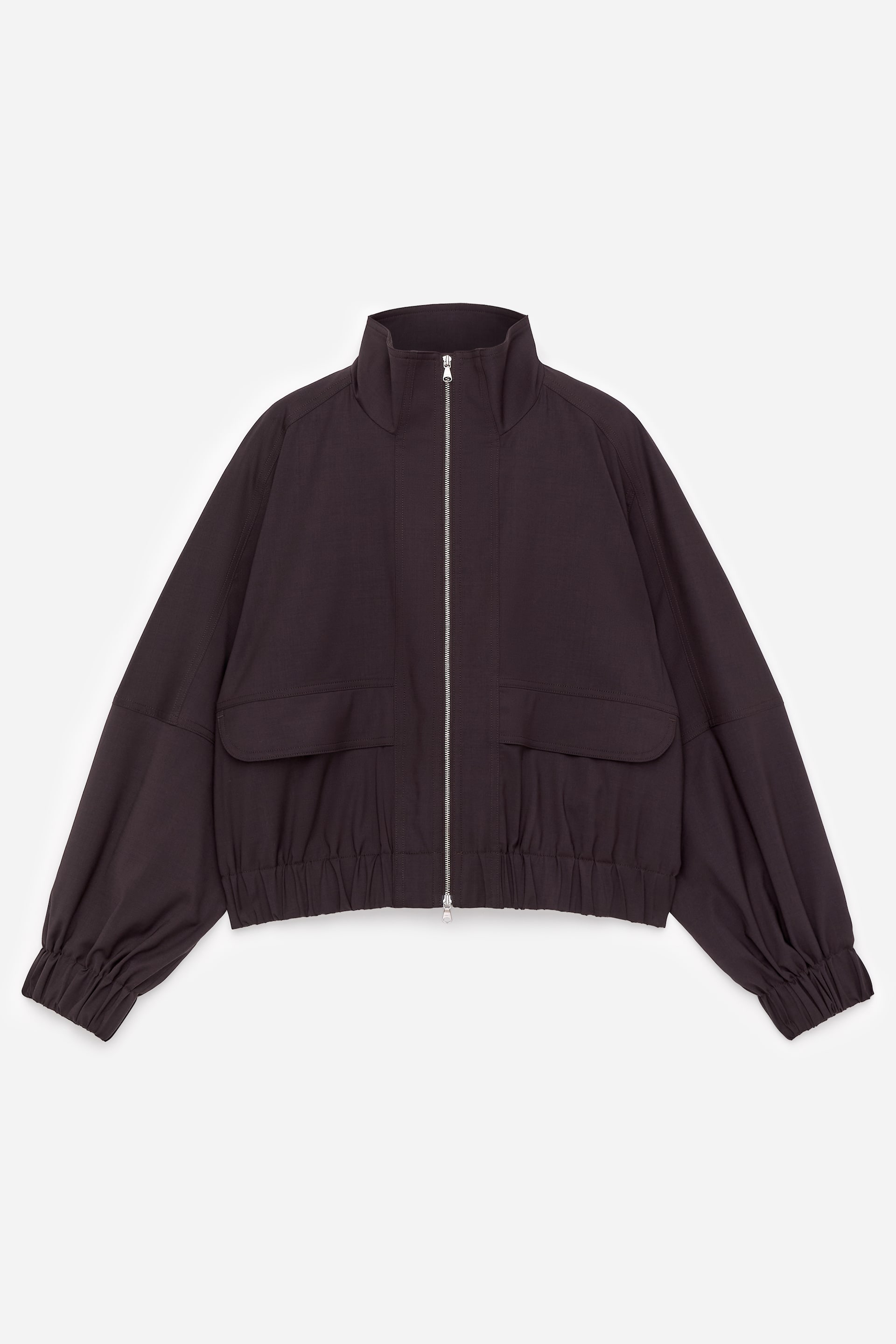 Grösseres Bild ansehen: Eine dunkelbraune Jacke wird von vorne gezeigt, mit einem Stehkragen und einem durchgehenden silberfarbenen Reißverschluss. Zwei große Klappentaschen zieren die untere Vorderseite, während geraffte Bündchen und ein geraffter Saum die Ärmel und die Taille betonen.