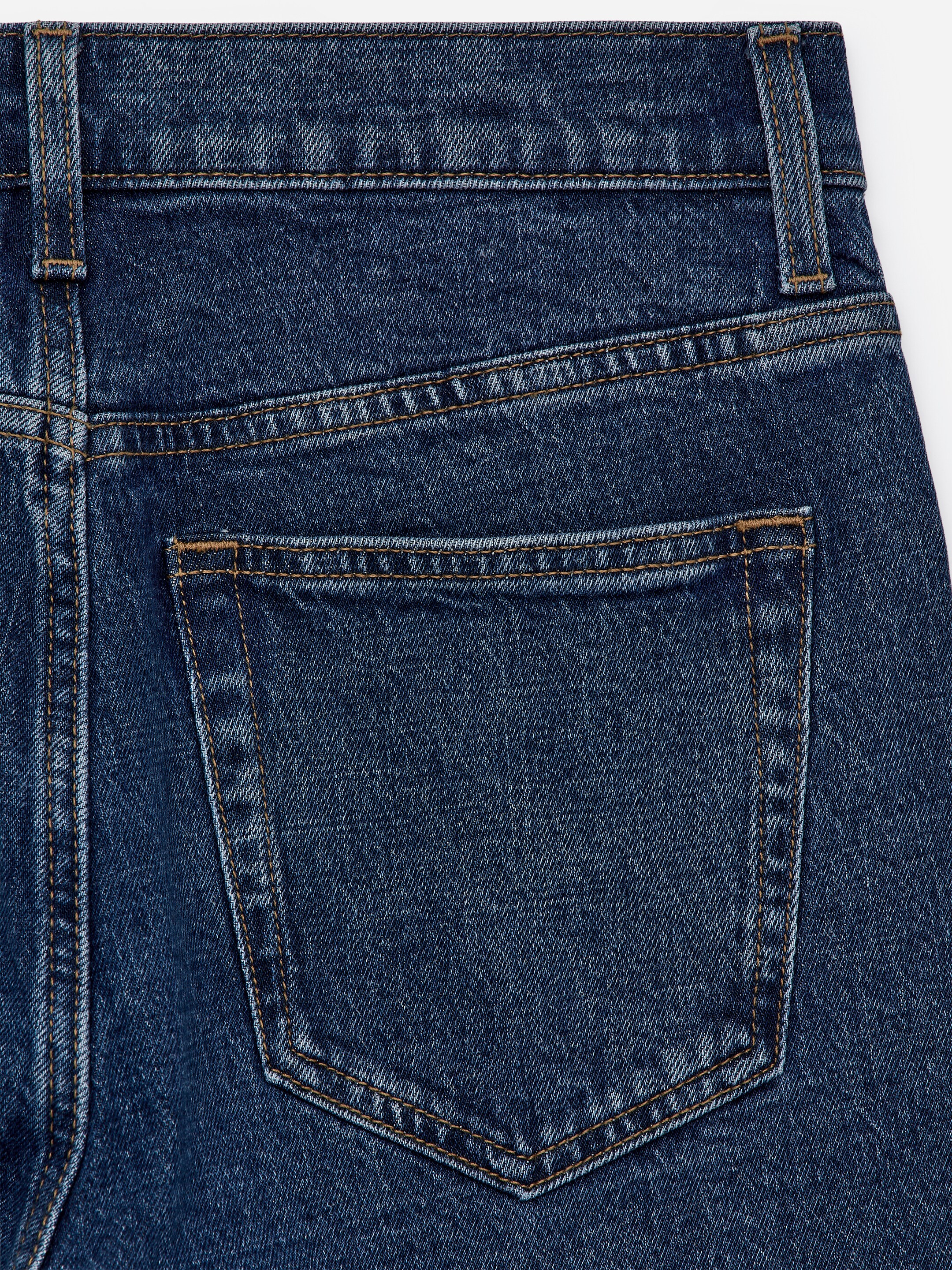 Visualizza immagine più grande: Il retro di un jeans in denim blu scuro è visibile, con una tasca applicata, un carré distintivo e passanti per cintura, tutti delineati con cuciture a contrasto arancioni.