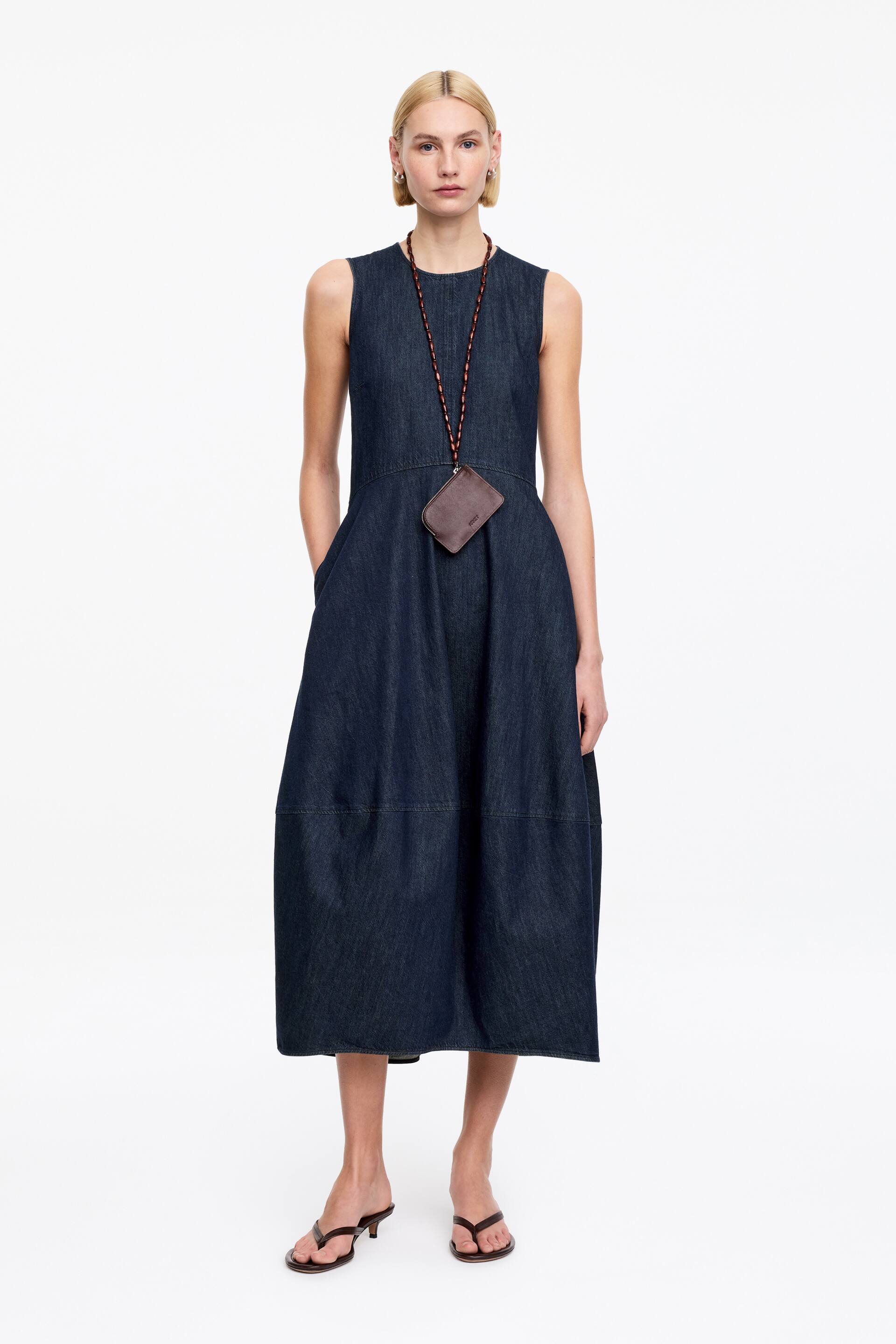 Agrandir l'image: Robe midi en denim délavé foncé avec un design sans manches, une silhouette structurée en ligne A avec des détails de coutures en panneaux, et des poches latérales intégrées.