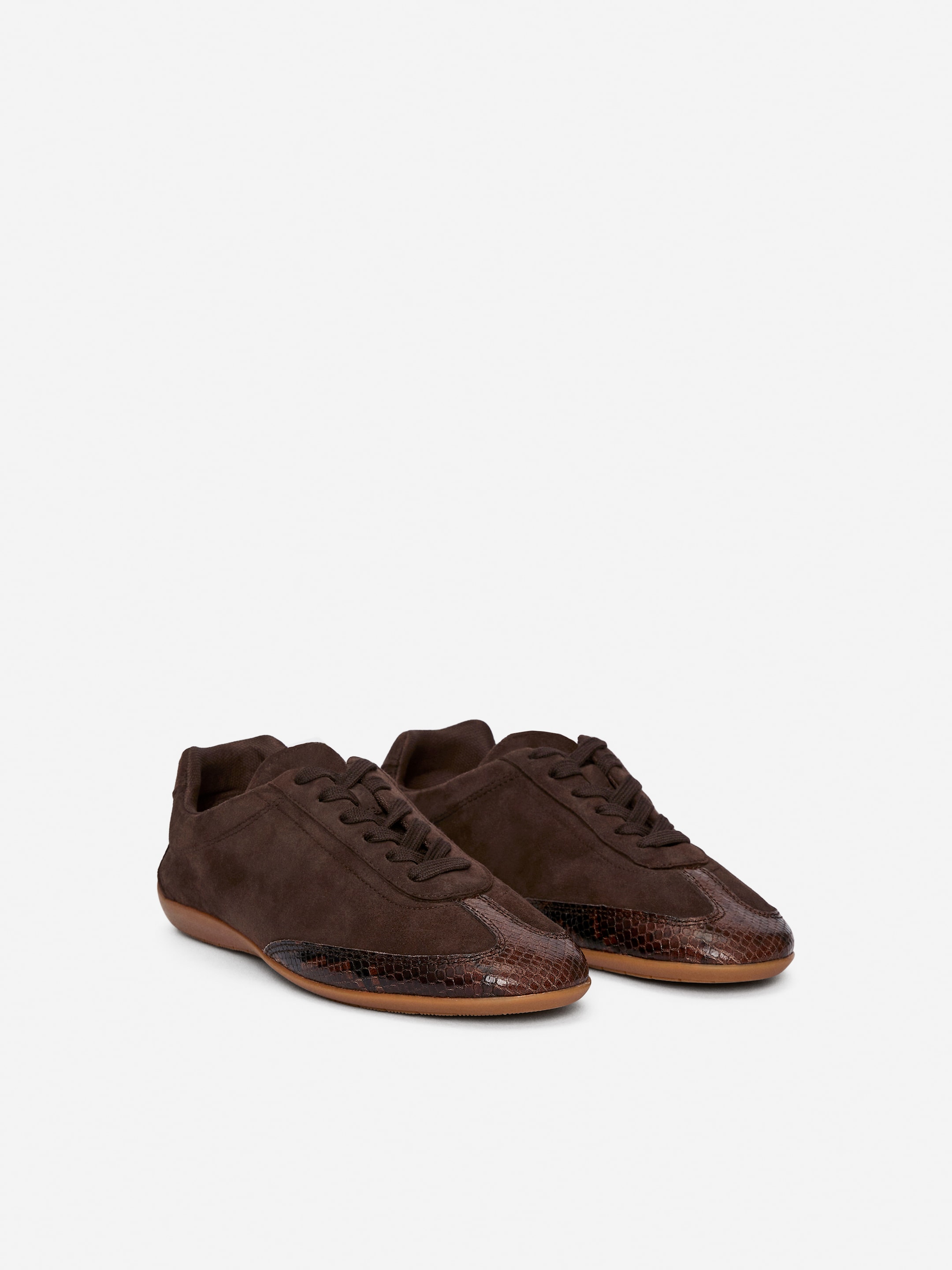 View larger image: Front-facing dark brown trainers are being presented, crafted from suede with a streamlined silhouette. They are featuring lace-up fastenings and textured panels on the toe and forefoot, resting on a light brown sole.