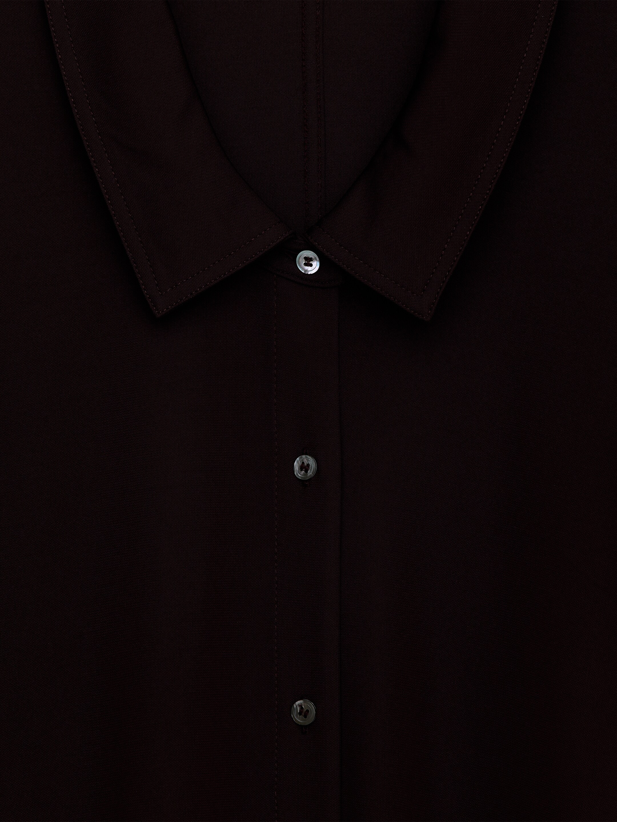 Ver imagem maior: Uma camisa castanha escura está a exibir a sua gola pontiaguda com pesponto visível e uma carcela frontal de botões. Botões leves e iridescentes, semelhantes a conchas, estão a assegurar a carcela.