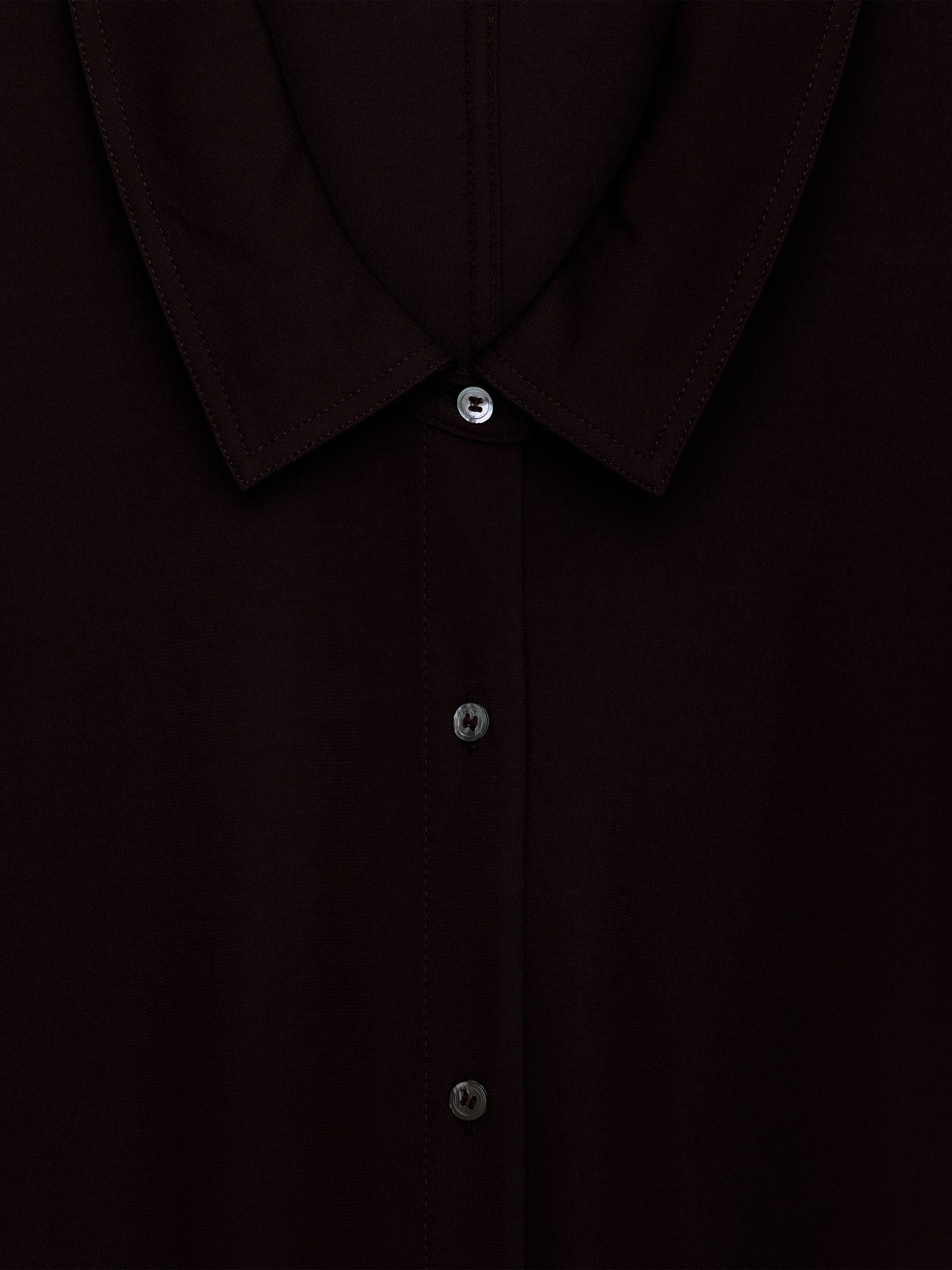 Agrandir l'image: Une chemise marron foncé met en valeur son col pointu avec une surpiqûre visible et une patte de boutonnage à l'avant. Des boutons légers, iridescents et en forme de coquille sécurisent la patte de boutonnage.