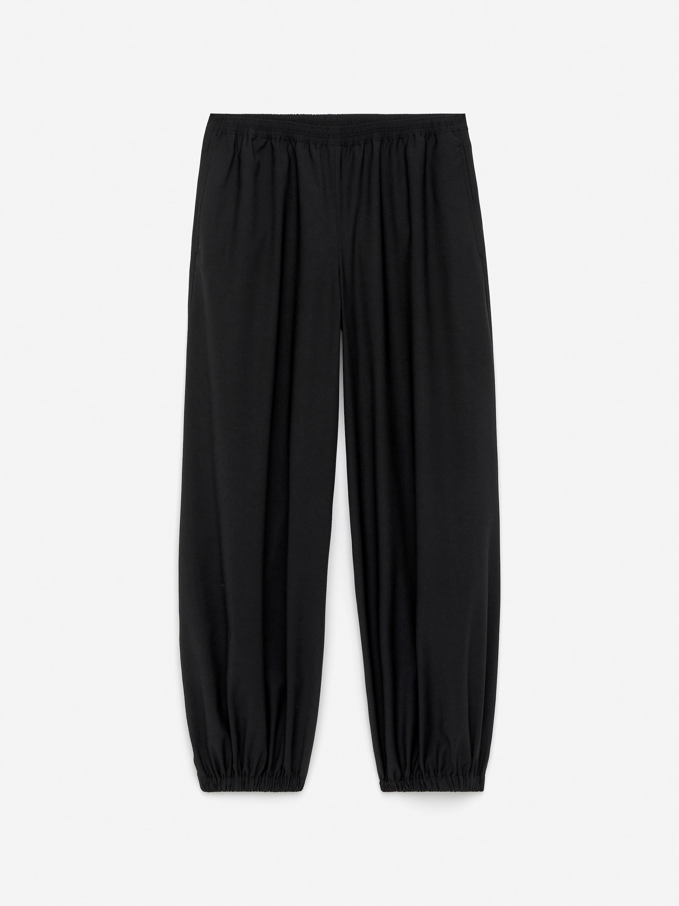 Grotere afbeelding bekijken: Zwarte broek wordt gepresenteerd vanuit een vooraanzicht, met een barrel-leg silhouet en een ontspannen pasvorm. Ze hebben een elastische tailleband, zijzakken en elastische boorden die bij de enkels samenkomen.
