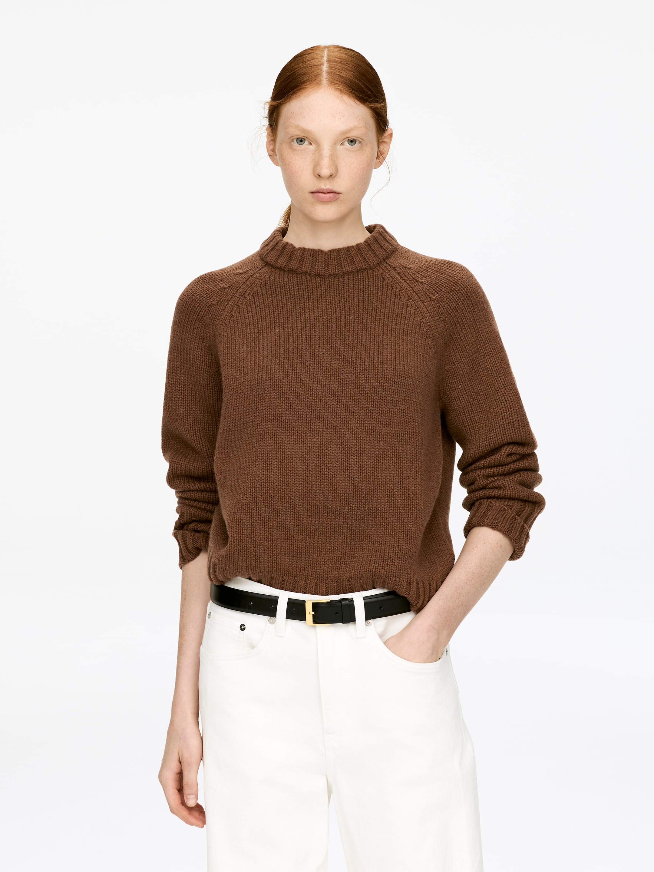 View larger image: The Chunky Pure Cashmere Jumper is being worn by the model. This brown, chunky knit garment features a high ribbed collar, raglan sleeves, and ribbed cuffs, and is styled over white trousers.
