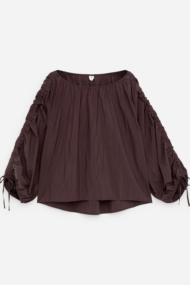 Un chemisier marron foncé est présenté de FACE, avec un large col froncé et une texture froissée. Ses manches longues affichent des détails froncés et des liens aux poignets. - 1