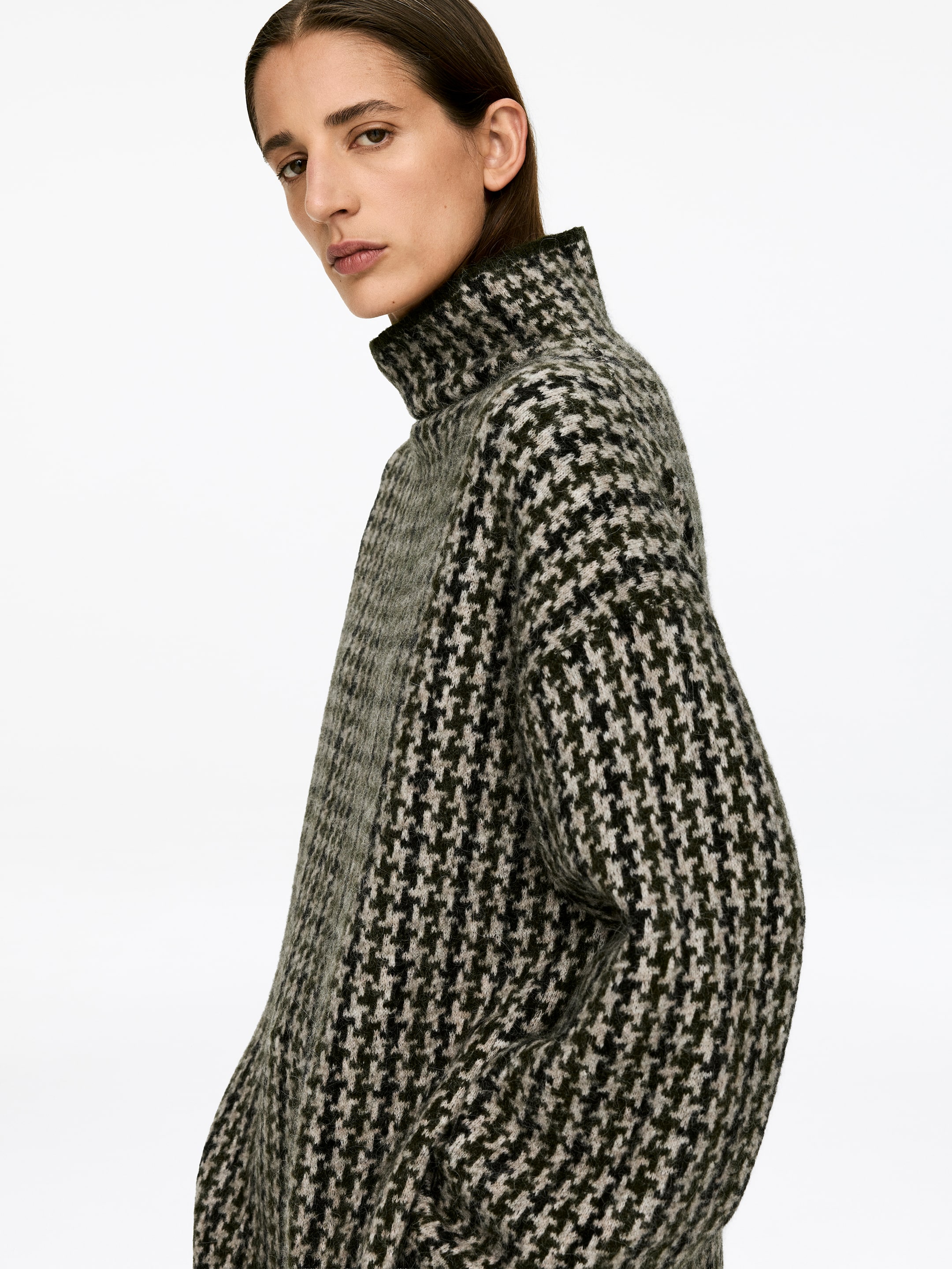 Visa större bild: En tröja med jacquard-stickning i ett mörkgrönt och ljusbeige hundtandsmönster bärs av modellen. Den har en högre halsringning, långa ärmar och en avslappnad passform.