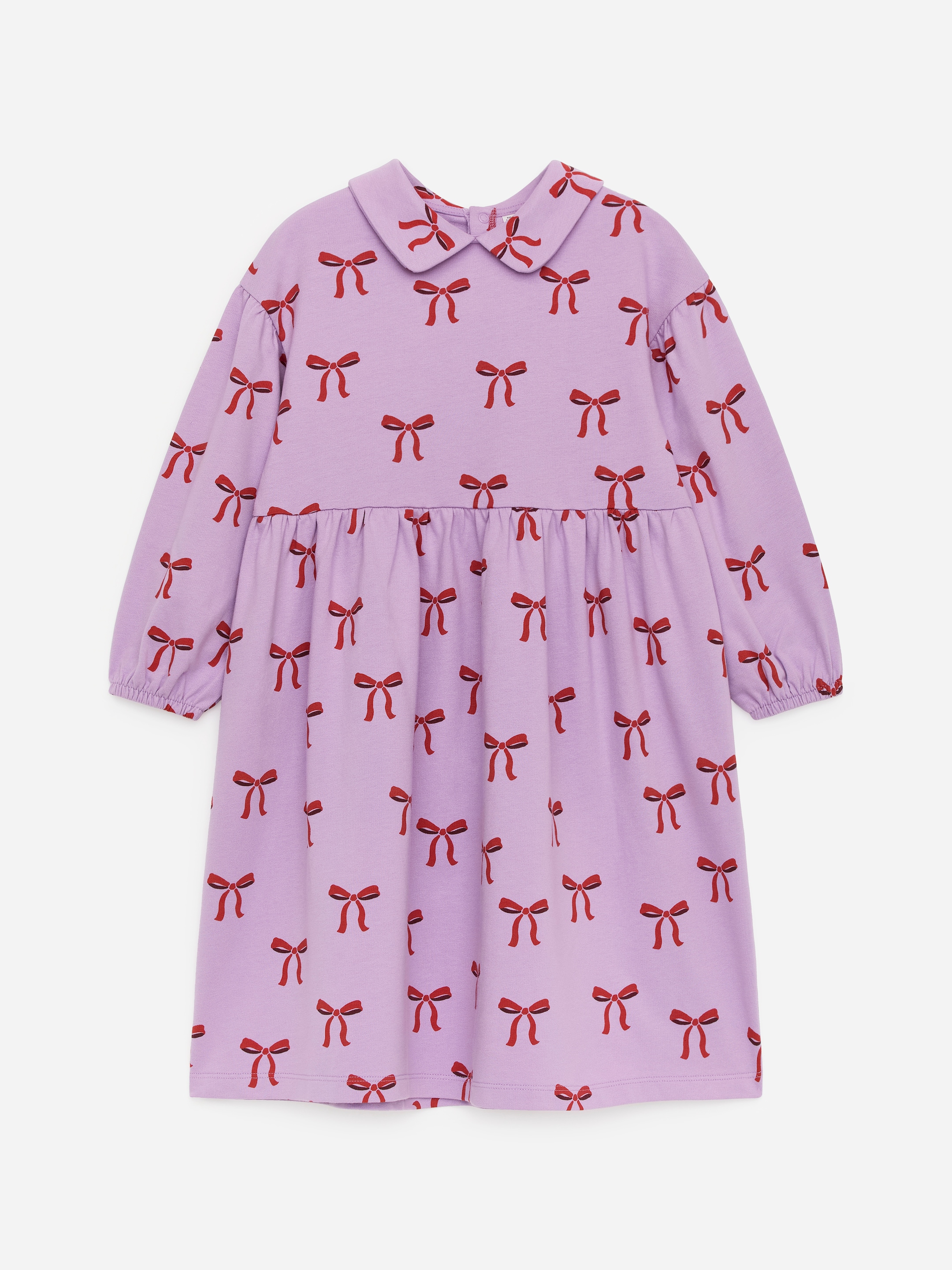 Προβολή μεγαλύτερης εικόνας: Ένα ανοιχτό μοβ φόρεμα με μακριά μανίκια παρουσιάζεται από μπροστά, με ένα κόκκινο σχέδιο φιόγκου σε όλη την επιφάνεια. Είναι σχεδιασμένο με στρογγυλεμένο γιακά Peter Pan, φούστα με πιέτες και ελαστικές μανσέτες.