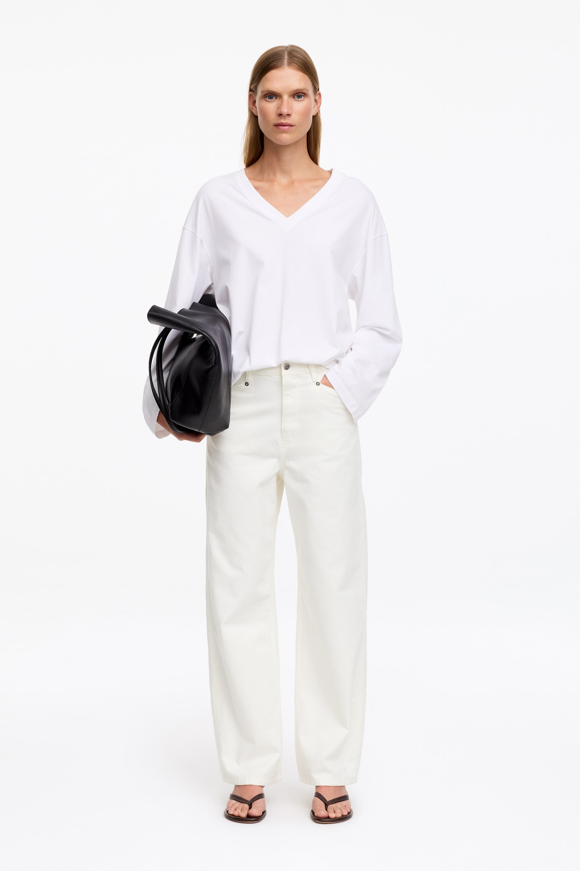 Größeres Bild anzeigen: Der/die Model trägt eine cremefarbene Baumwoll-Canvas-Hose mit regulärer Taille, relaxed Fit und Five-Pocket-Design. Das Model steht mit einer Hand in einer vorderen Hosentasche; dazu ist die Hose mit einem weißen Langarmhemd und dunklen Flip-Flops kombiniert.