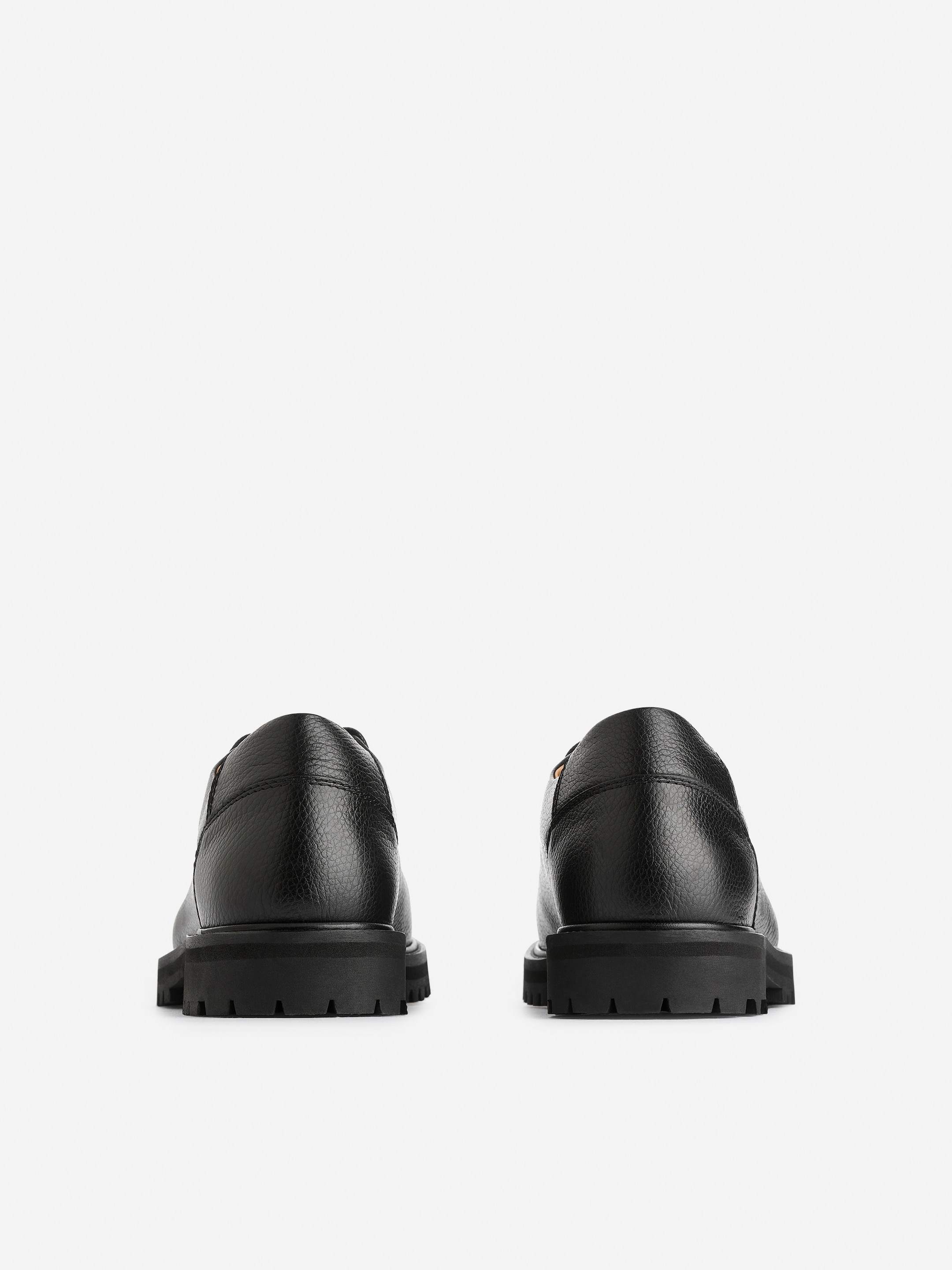 Grösseres Bild ansehen: Zwei schwarze Wanderschuhe sind nach hinten gerichtet und zeigen ihre genarbten Lederobermaterialien, gepolsterten Kragen und dicken Gummiprofilsohlen.