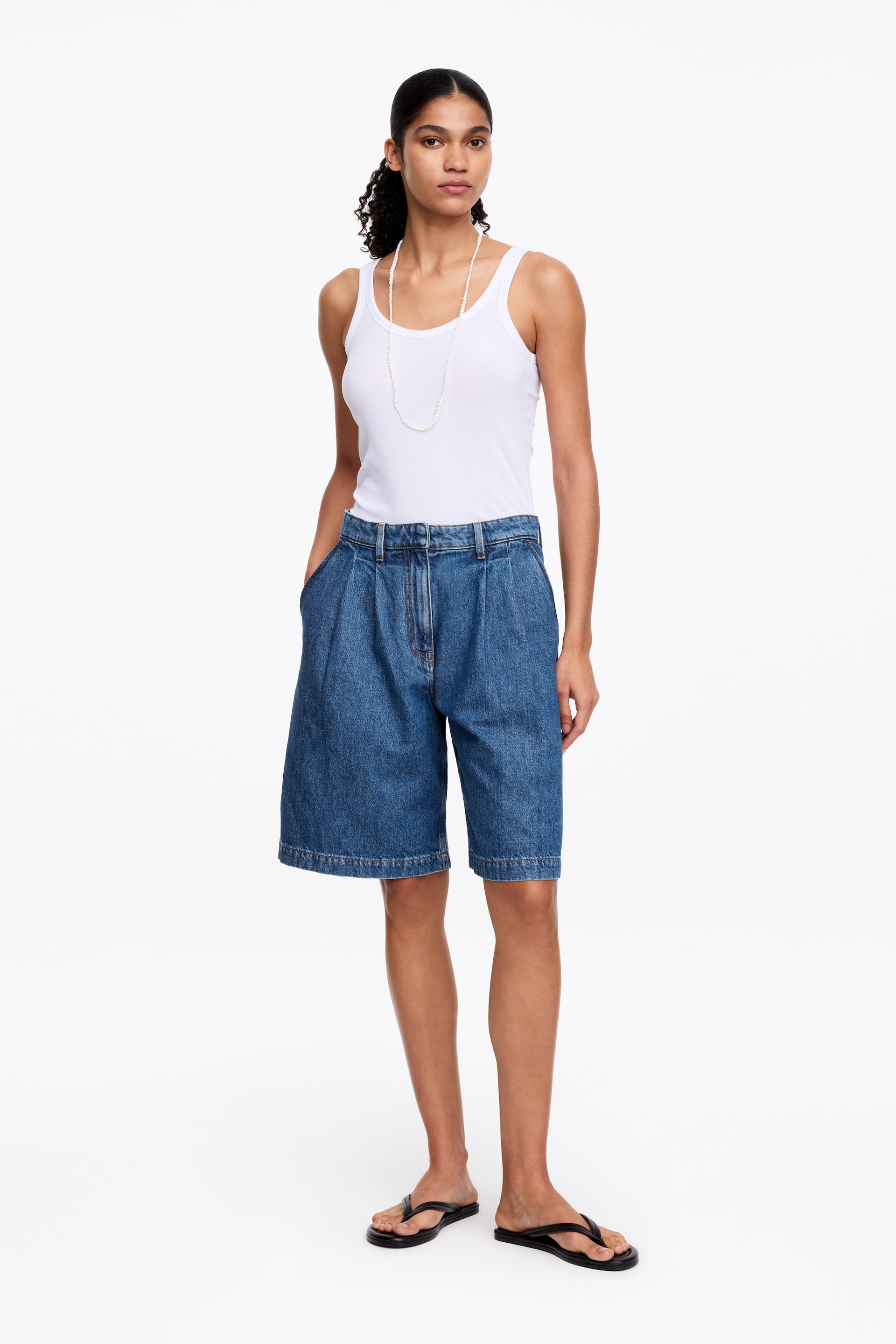 View larger image: A white vest top is showcased from a frontal perspective, featuring a round neckline and wide ribbed shoulder straps. The ribbed fabric fits closely to the torso and extends to the hip.