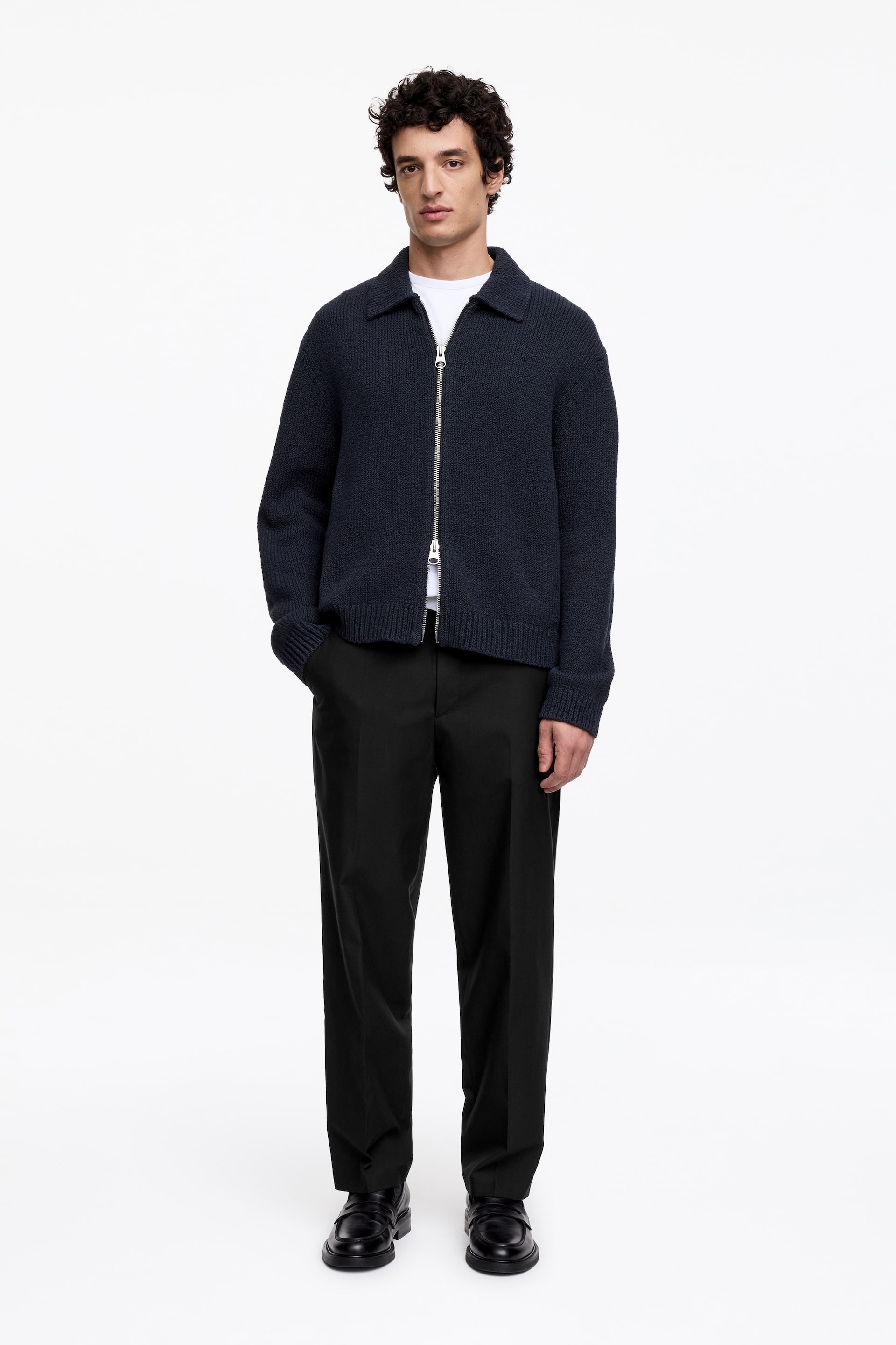 Grotere afbeelding bekijken: Een marineblauw gebreid jasje wordt frontaal getoond, open gedragen over een wit t-shirt. Een gespreide kraag omlijst de halslijn, een zilverkleurige ritssluiting loopt over het midden en geribbelde manchetten en zoom maken het ontwerp compleet.