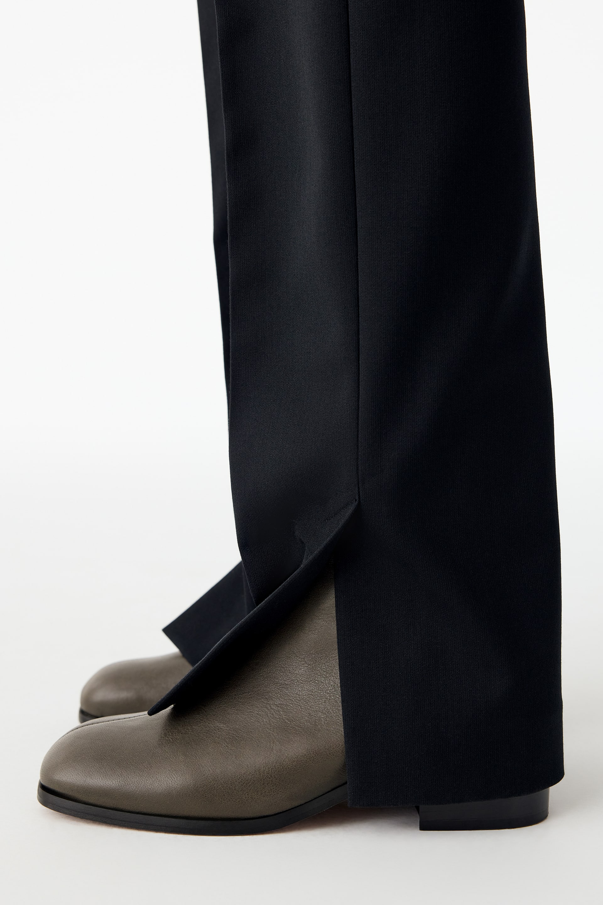 Visualizza immagine più grande: Stivaletti in pelle marrone oliva con punta squadrata e tacco largo basso indossati dalla modella. Gli stivaletti sono abbinati a pantaloni neri con orli anteriori spaccati che cadono sulle scarpe.