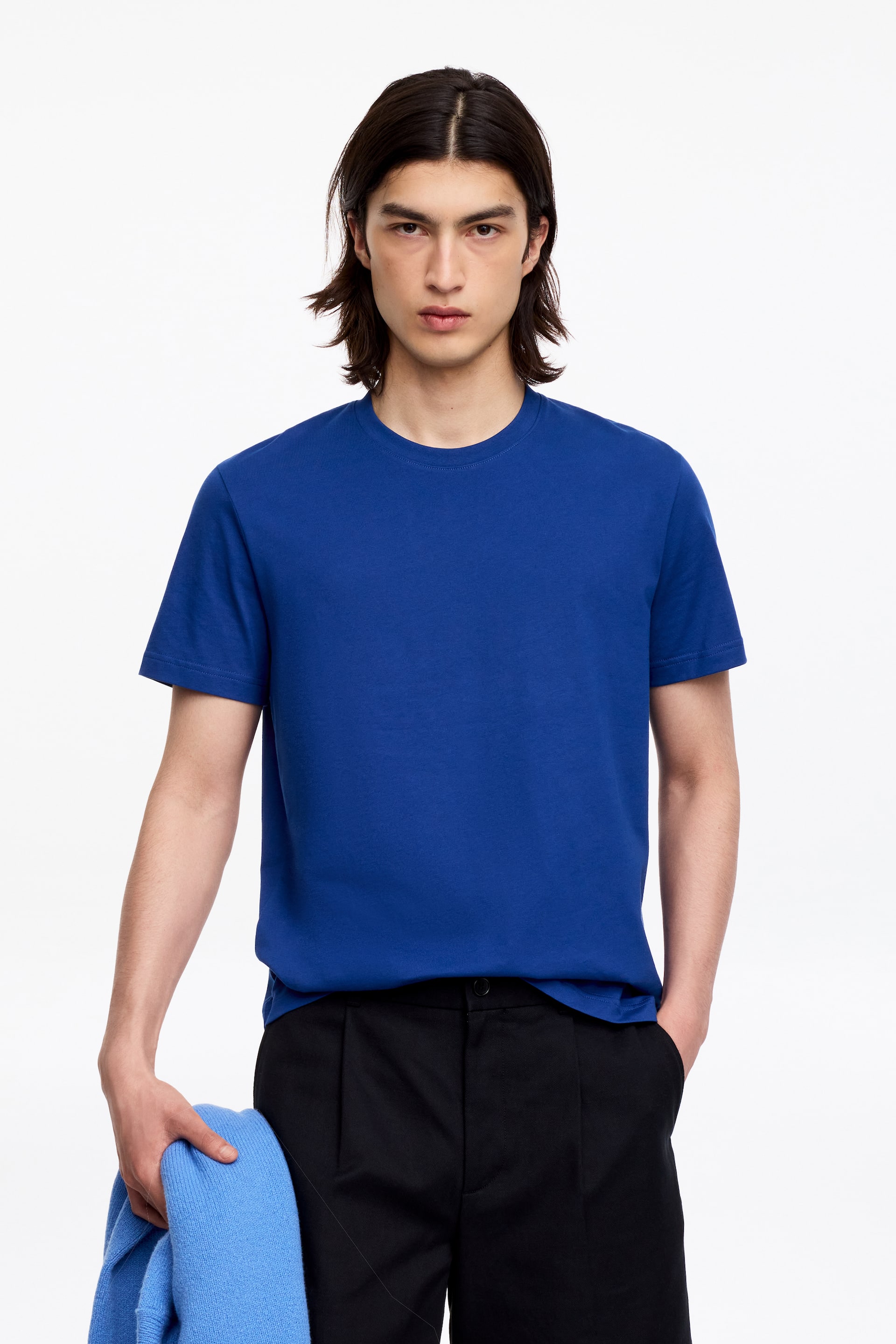 Visa större bild: En kungblå t-shirt presenteras, med rund hals och korta ärmar. Den har en klassisk passform, med rak fåll delvis instoppad i svarta byxor på ena sidan.