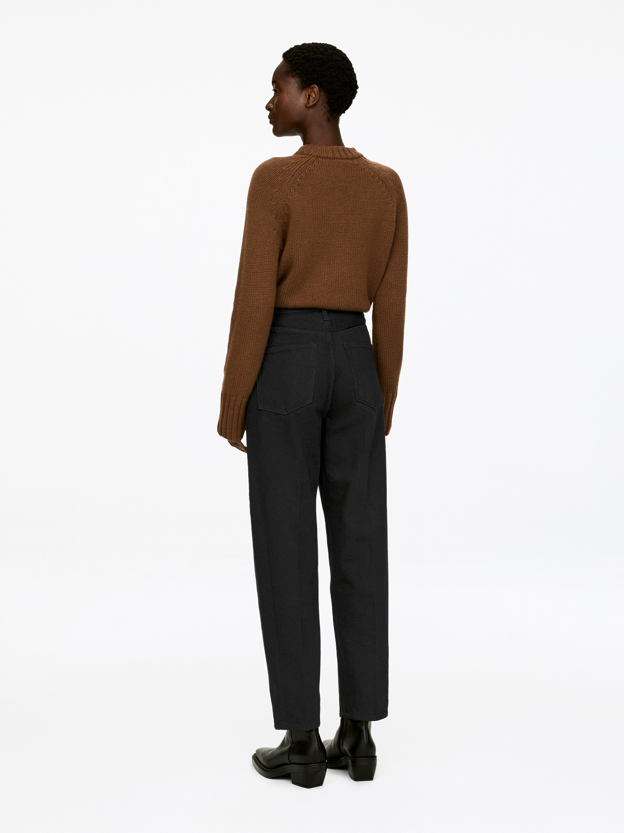 Agrandir l'image: Un pull en tricot marron avec des manches raglan, un col rond et des poignets et un ourlet côtelés est présenté de vue arrière trois quarts. Il est associé à un pantalon taille haute foncé, au style décontracté et à jambes droites, s'arrêtant juste au-dessus des bottines noires.